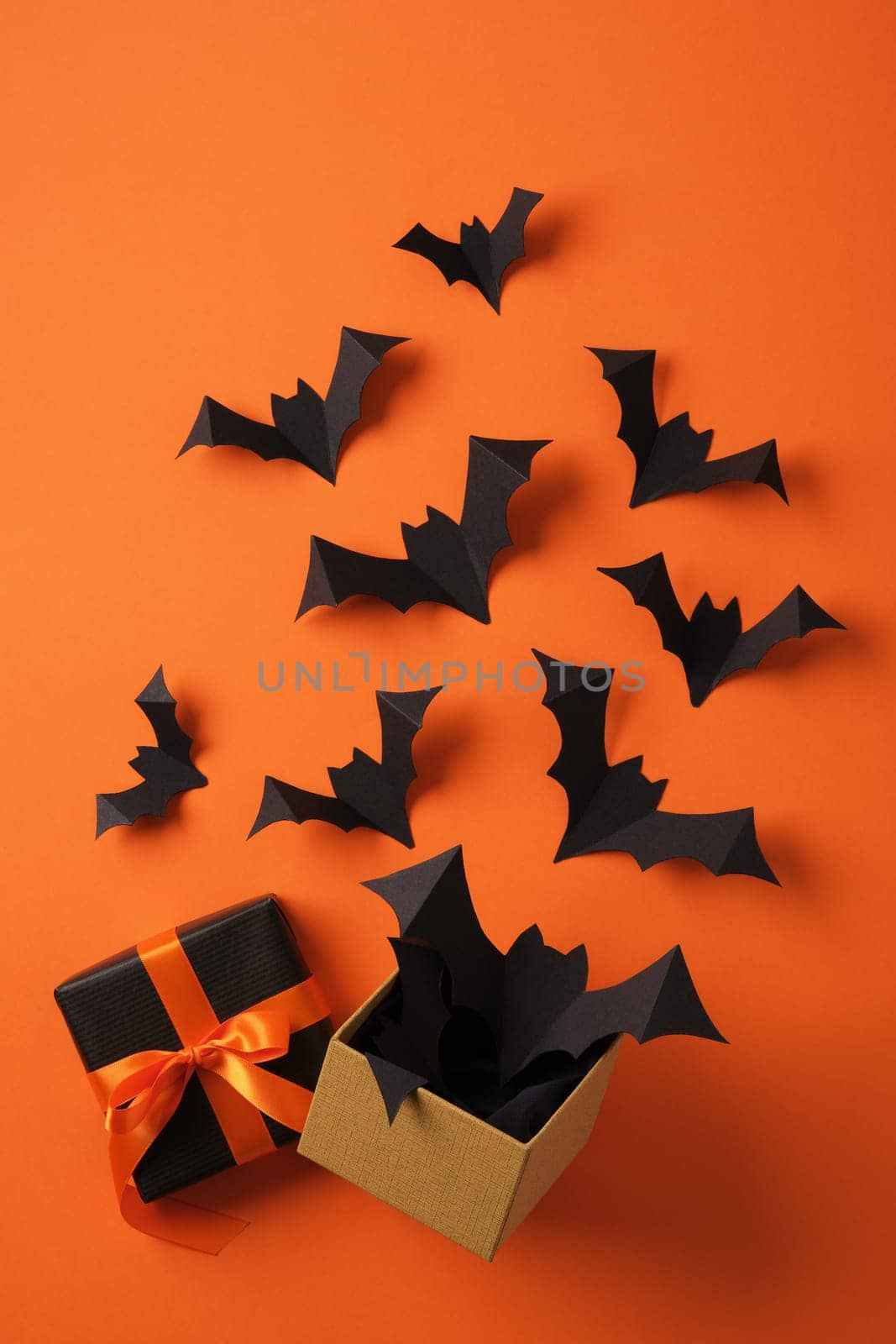 Paper bats flying out of gift box on orange backdrop. Background for Halloween cards, banners, invitations.