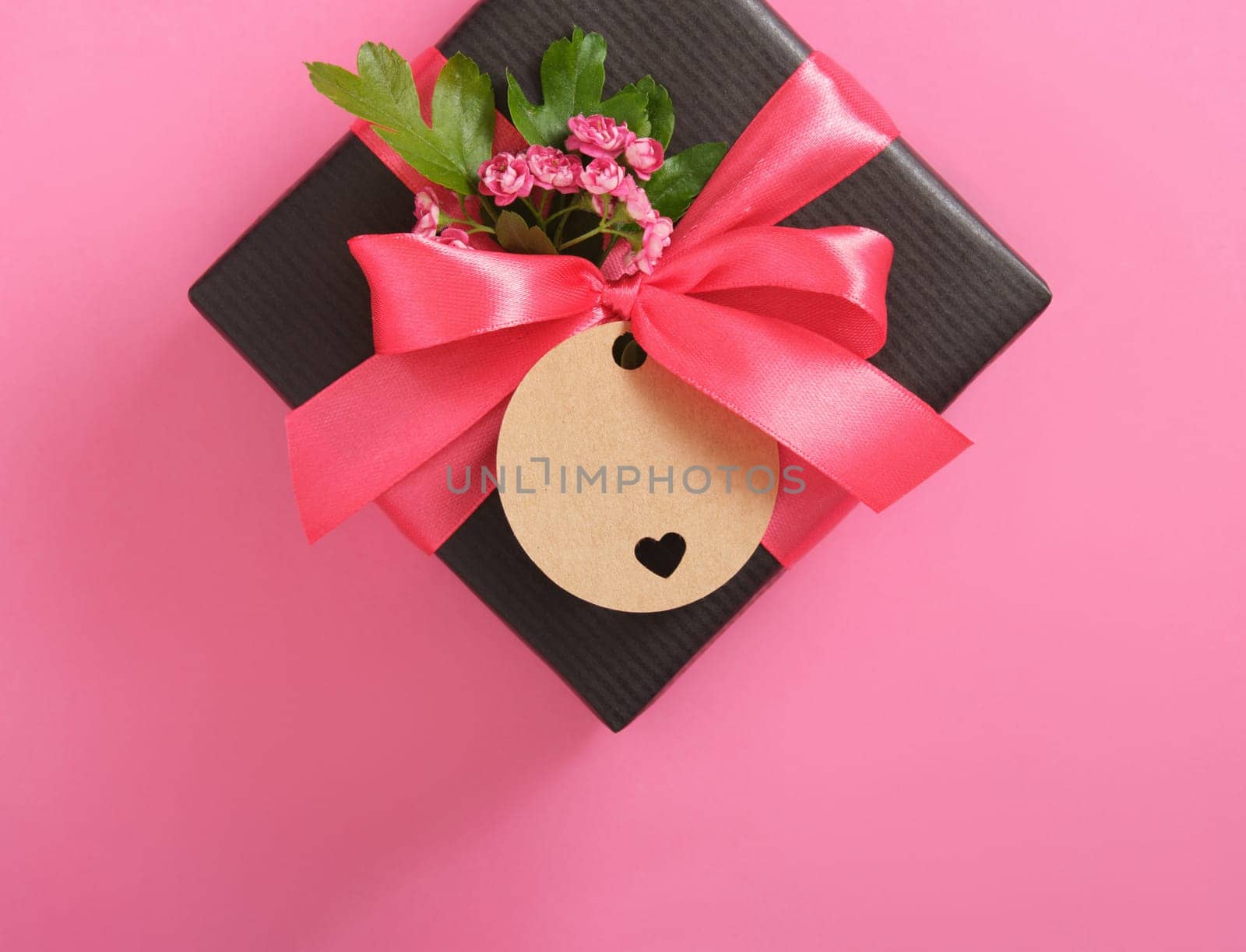 Black craft gift box with empty tag, hawthorn flowers on pink background. Place for your text
