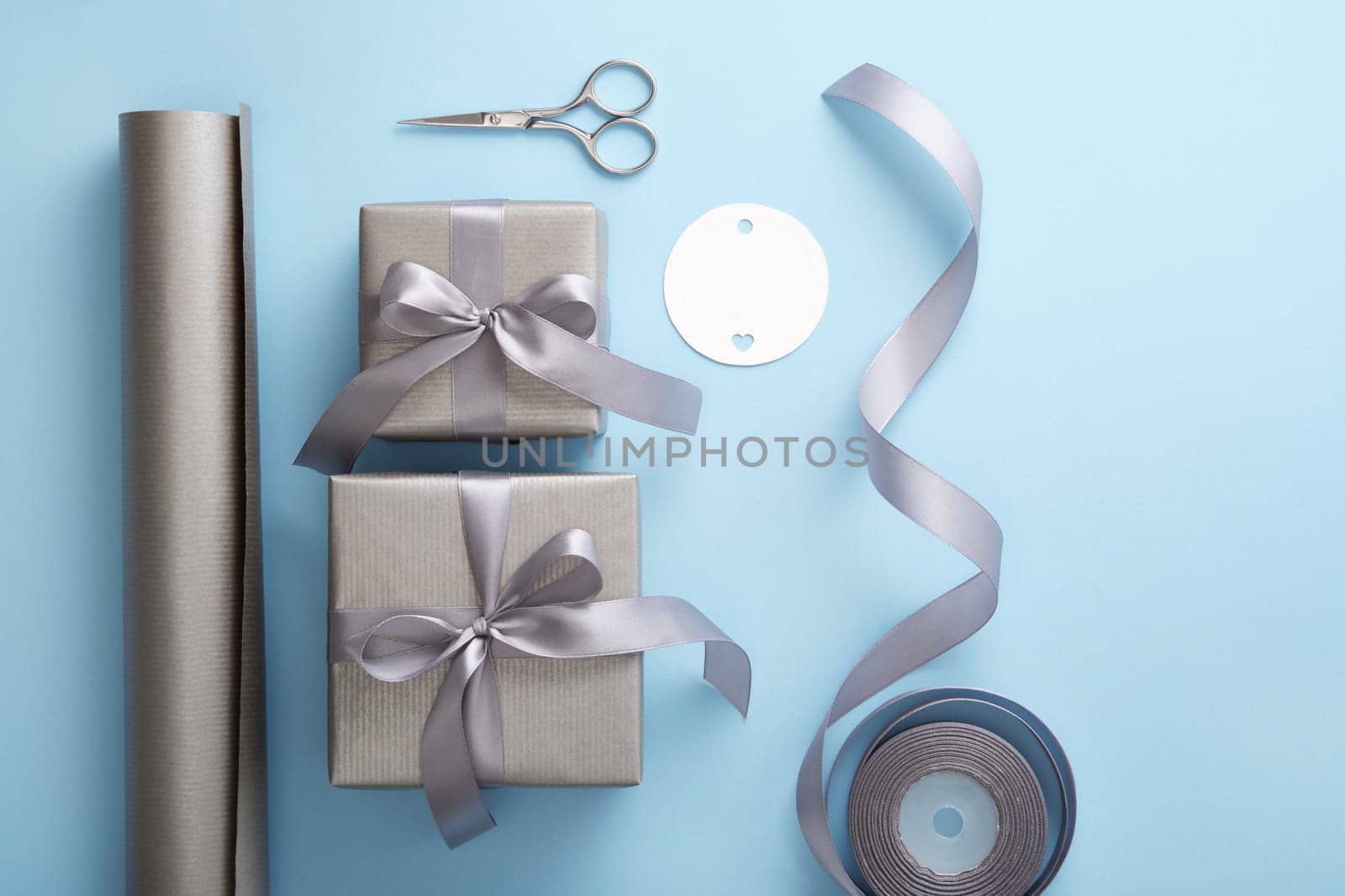 Gift wrapping. Gray wrapping paper, silver ribbon, scissors on light blue background