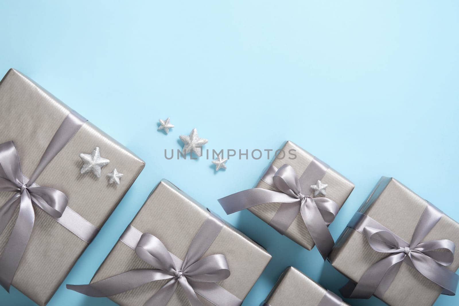 Set of monochrome gray gift boxes with gray ribbons and silver stars on light blue background. Copyspace