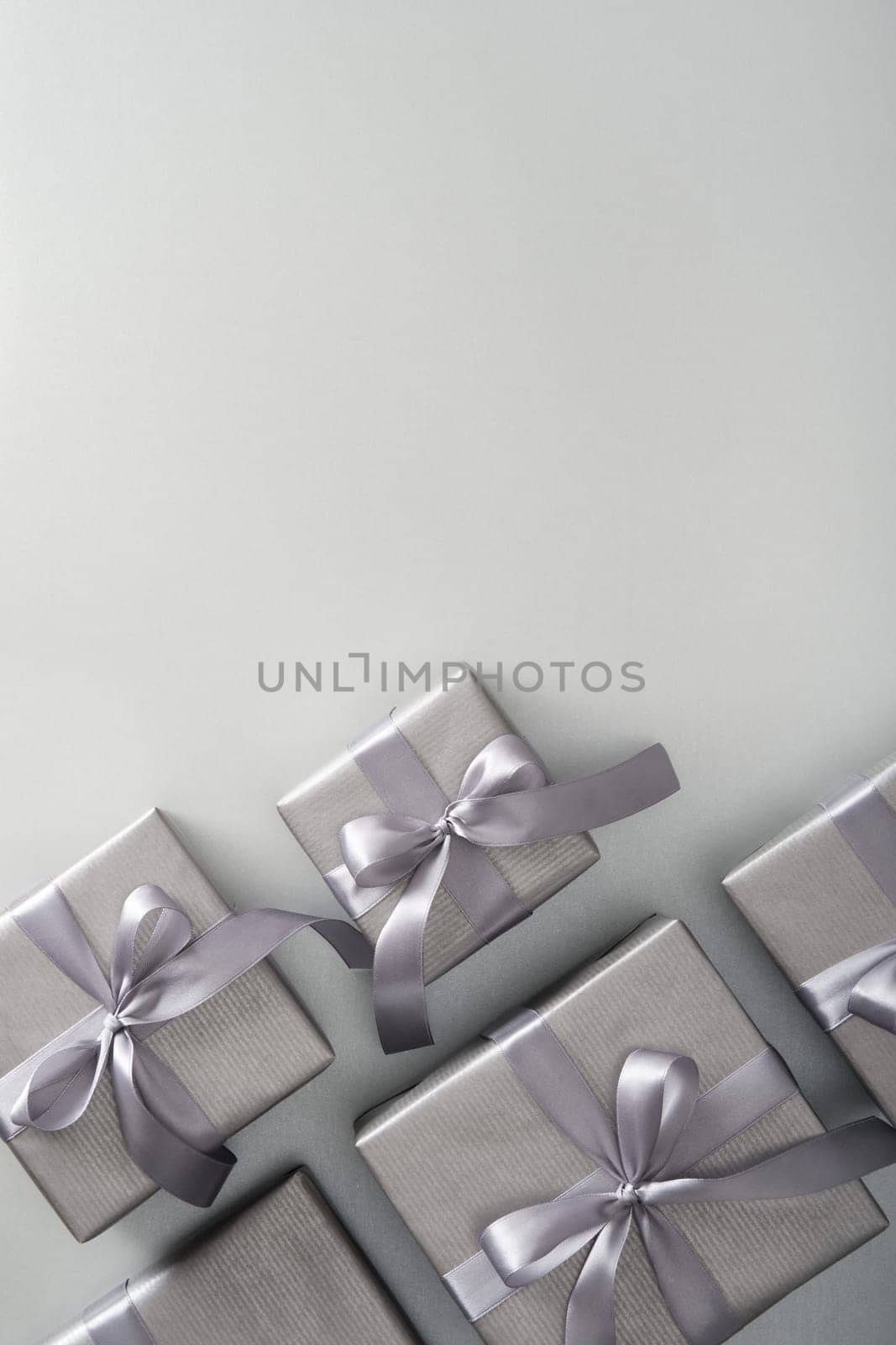 Silver gift boxes with gray ribbons on light background. Vertical, space for your text.
