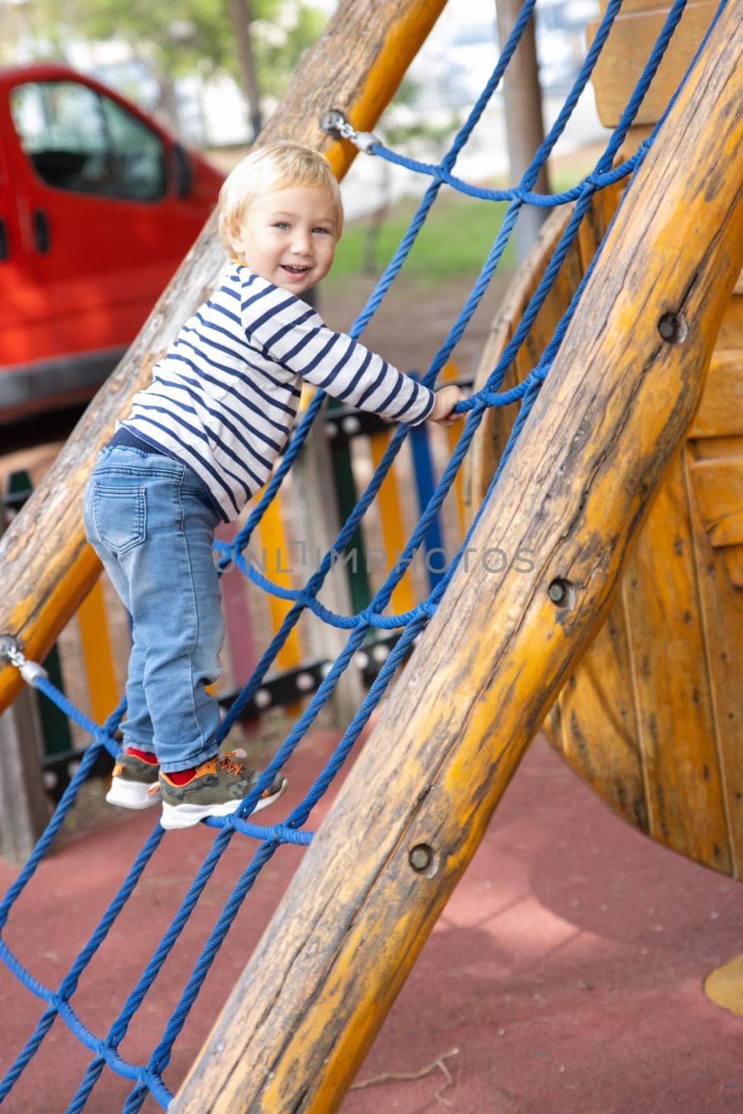 Cute little blonde boy playing on the playground - looking in the camera. Vertical shot
