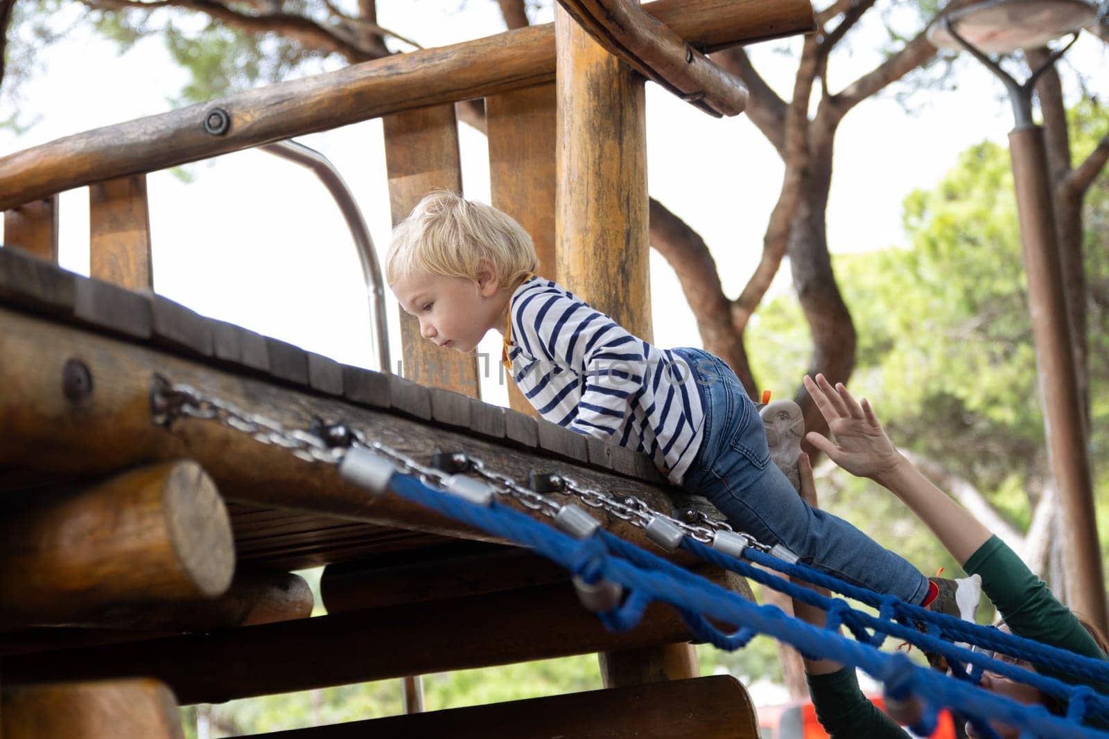 A little boy climbs ropes on a wooden installation at the playground. Mid shot
