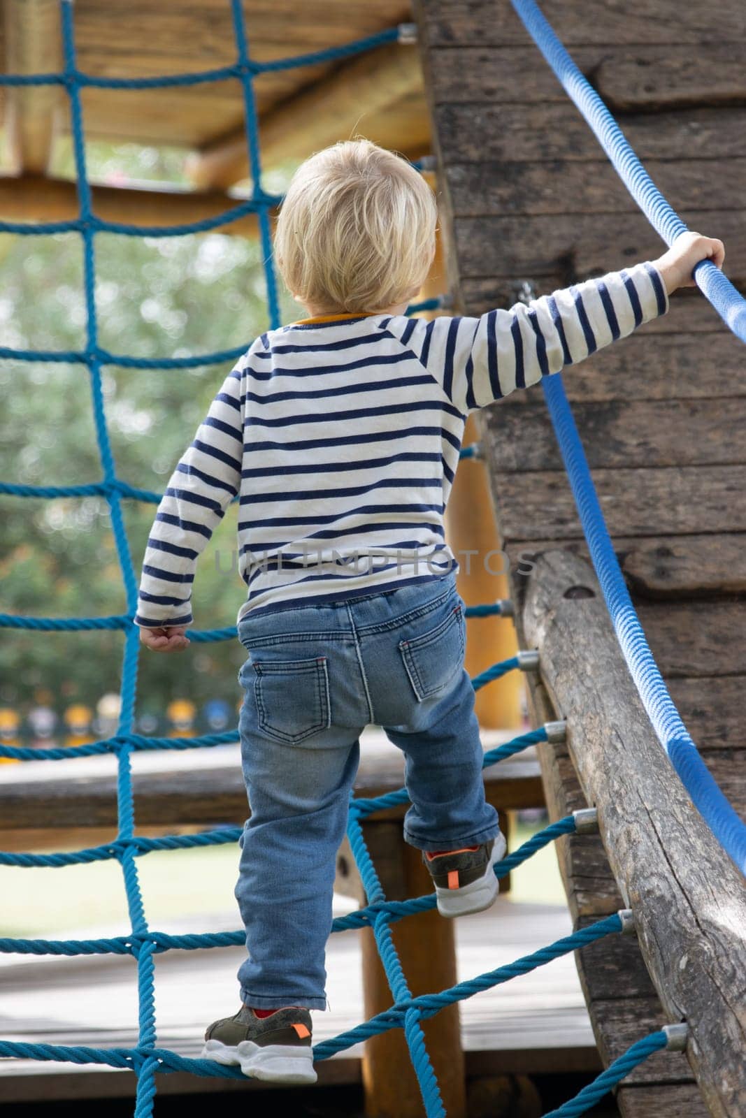 Little boy walking up a rope ladder on the playground. Vertical shot