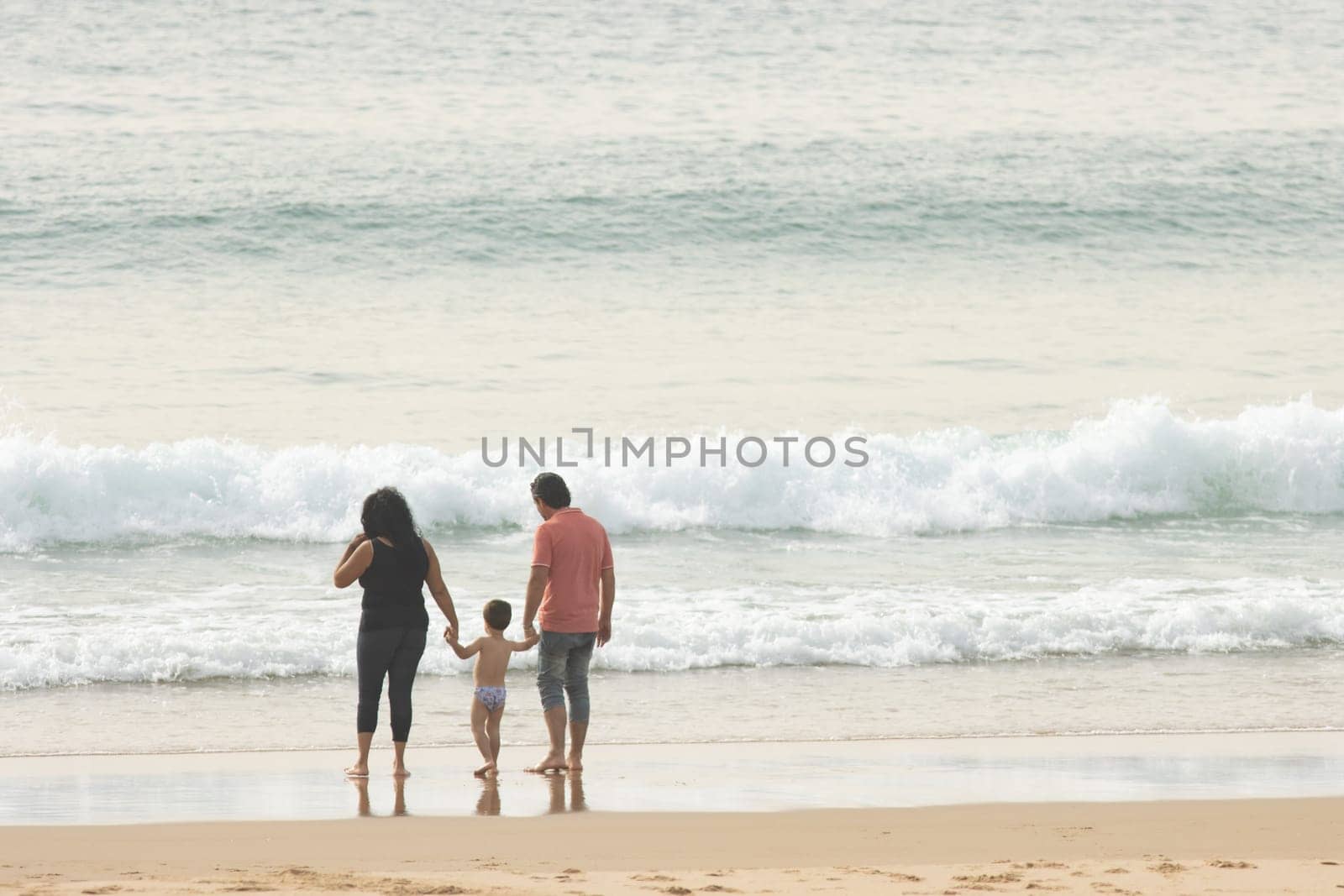 A family of mom, dad and little son stands on the beach by the sea. Mid shot