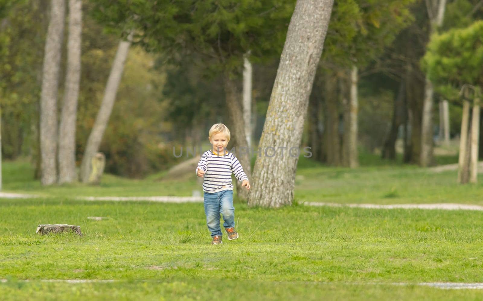 Cute smiling blonde boy running on the green field. Mid shot
