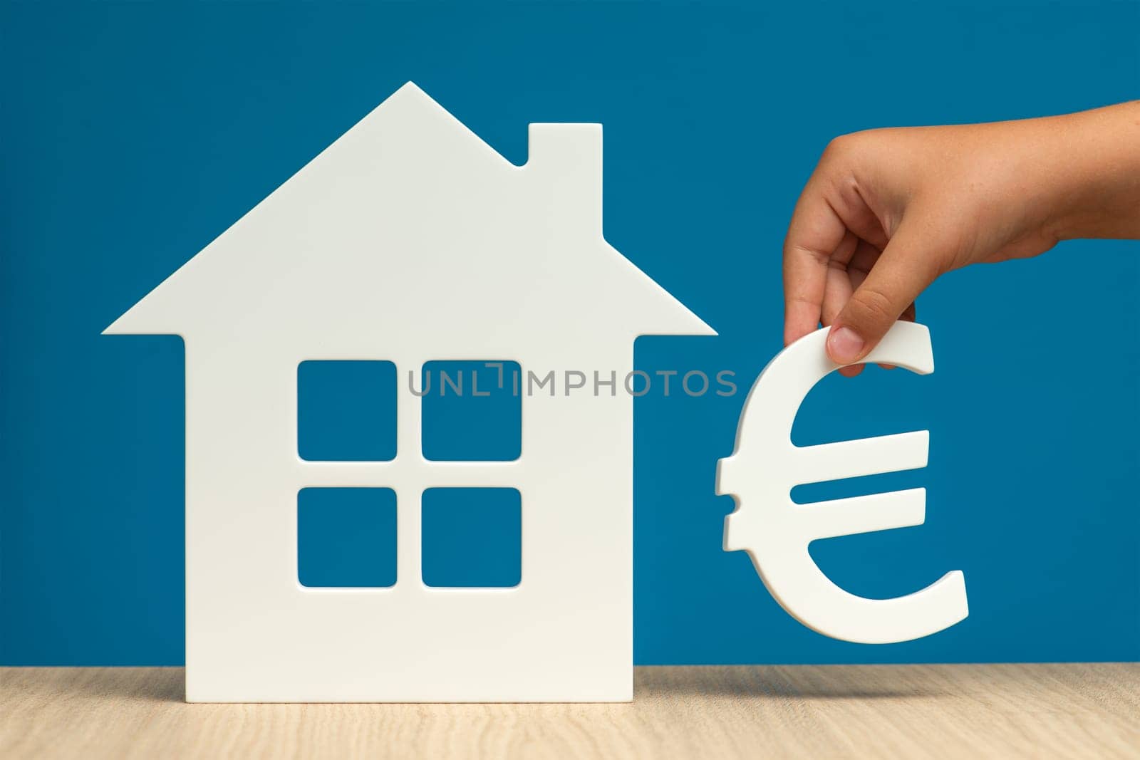 The cost of renting real estate in Europe. Renting residential real estate in the European Union. Model of a white house and a hand with a euro symbol on a blue background close-up. copy space by SERSOL