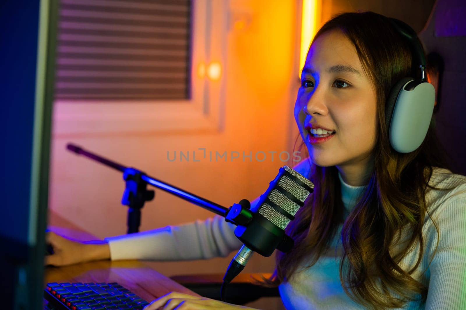 Asian young gamer woman playing video games online on computer she live stream and chat with fans, Happy streamer female talking with microphone in gaming room, game streaming concept