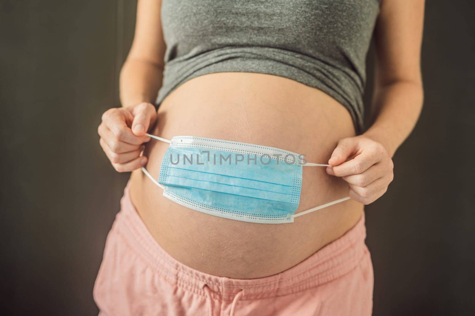 Belly of a pregnant woman holding medical mask close up.