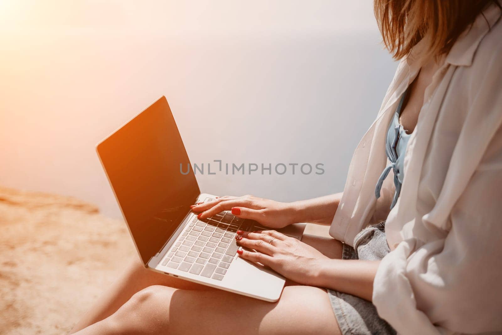 Woman sea laptop. Successful business woman working on laptop by the sea. Pretty lady typing on computer at summer day outdoors. Freelance, digital nomad, travel and holidays concept. by panophotograph