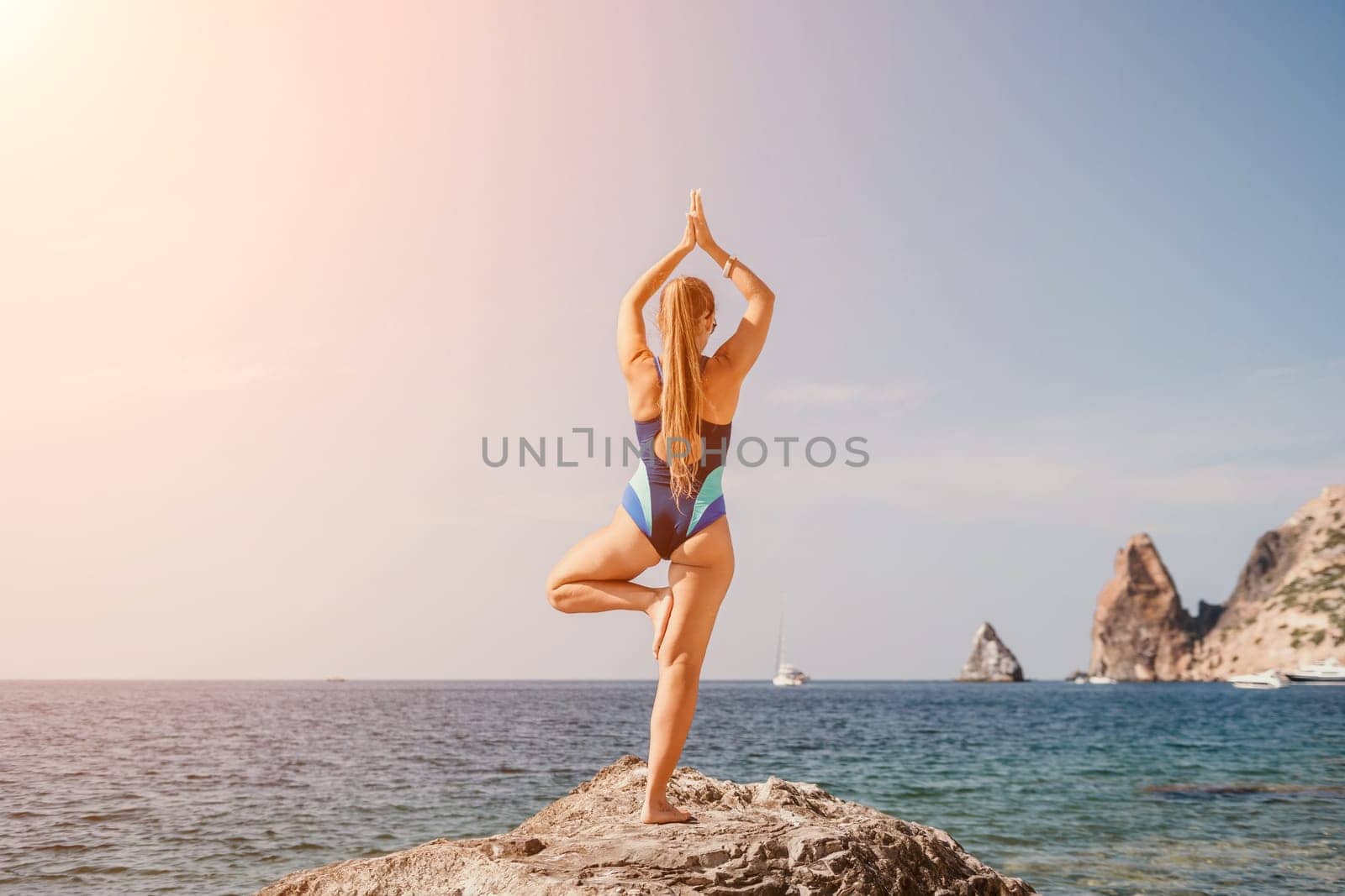 Woman sea yoga. Back view of free calm happy satisfied woman with long hair standing on top rock with yoga position against of sky by the sea. Healthy lifestyle outdoors in nature, fitness concept.