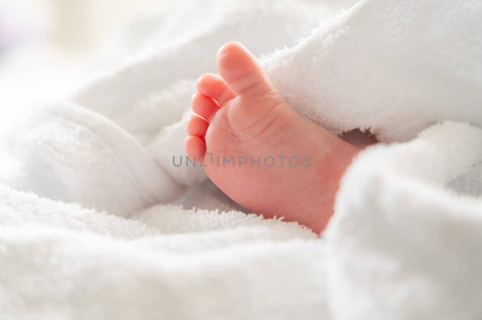 Tiny newborn foot peeking out after bath beneath soft white towel by Mariakray