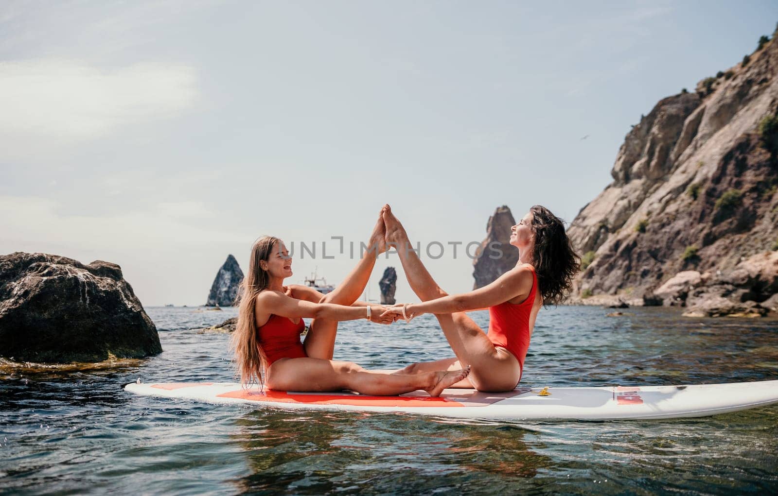 Woman sup yoga. Two happy sporty women practising yoga pilates on paddle sup surfboard. Female stretching doing workout on sea water. Modern individual female hipster outdoor summer sport activity. by panophotograph