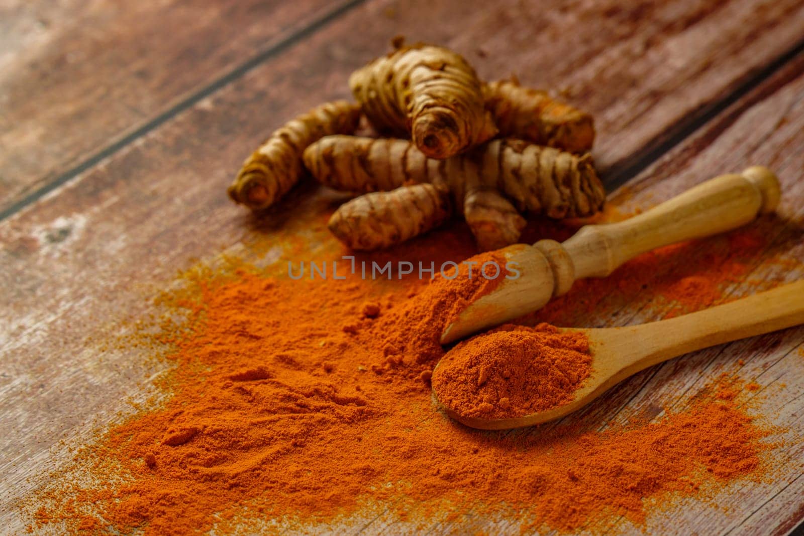 fresh turmeric root and ground turmeric in a wooden spoon poured out on a wooden table