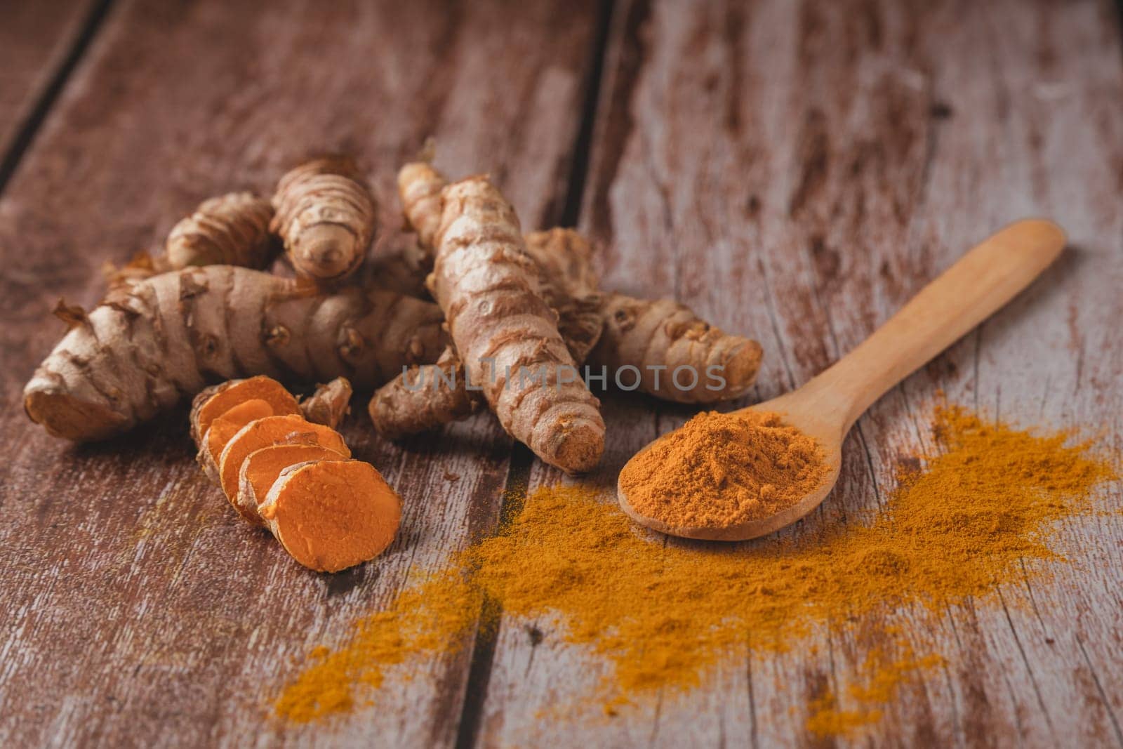 fresh turmeric root and ground turmeric in a wooden spoon by joseantona