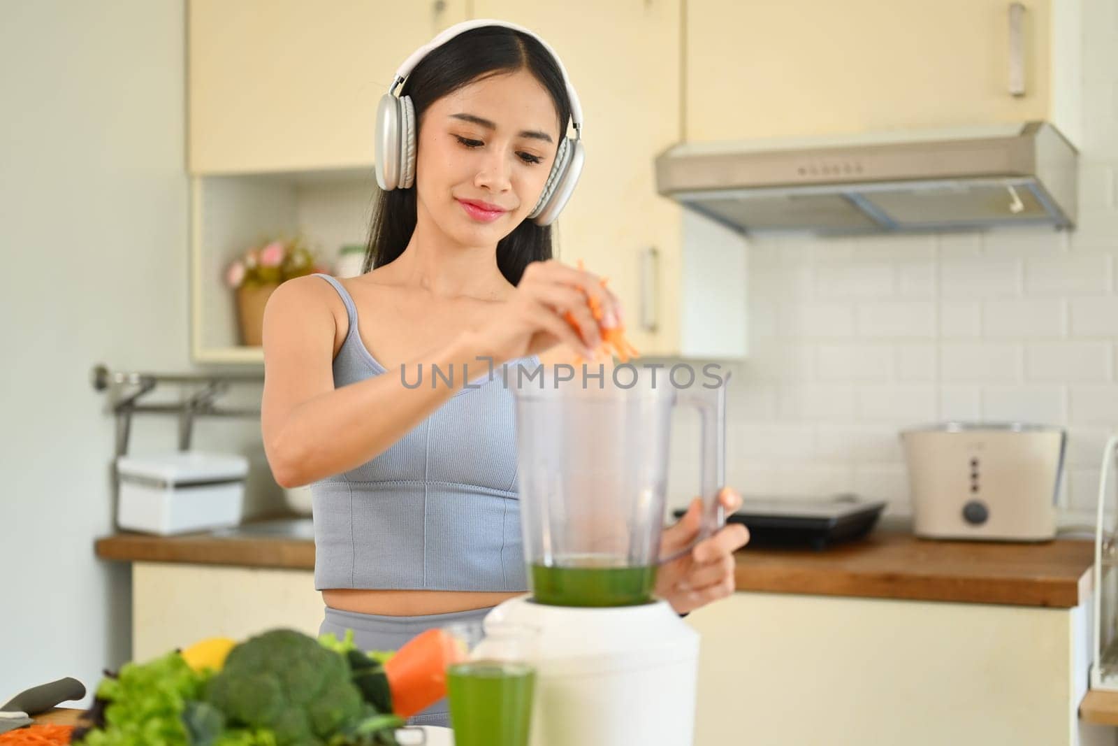 Happy young woman making healthy green smoothie with blender in kitchen. Healthy lifestyle concept by prathanchorruangsak