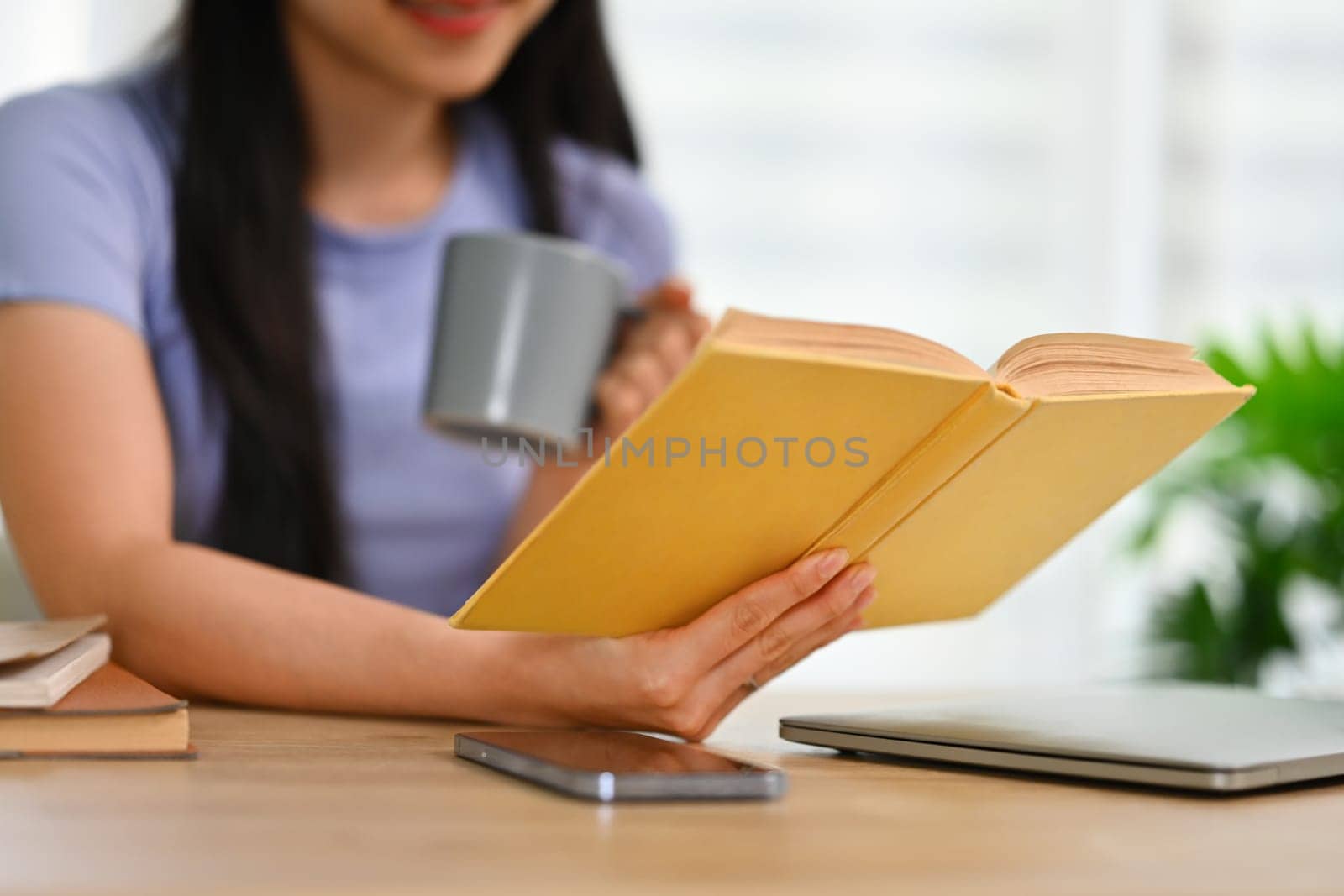 Calm young woman drinking tea and reading book at home. Education, knowledge and leisure activity concept.