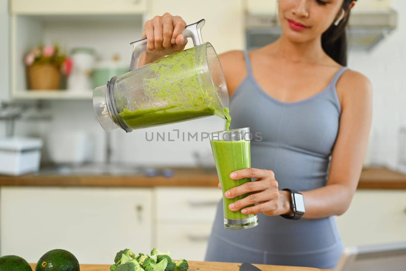 Young sporty woman pouring green detox smoothie into glass. Dieting and healthy lifestyle concept by prathanchorruangsak