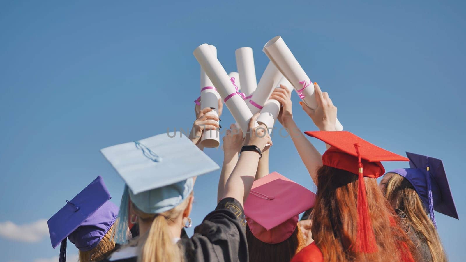 Graduates raise up their diplomas standing together