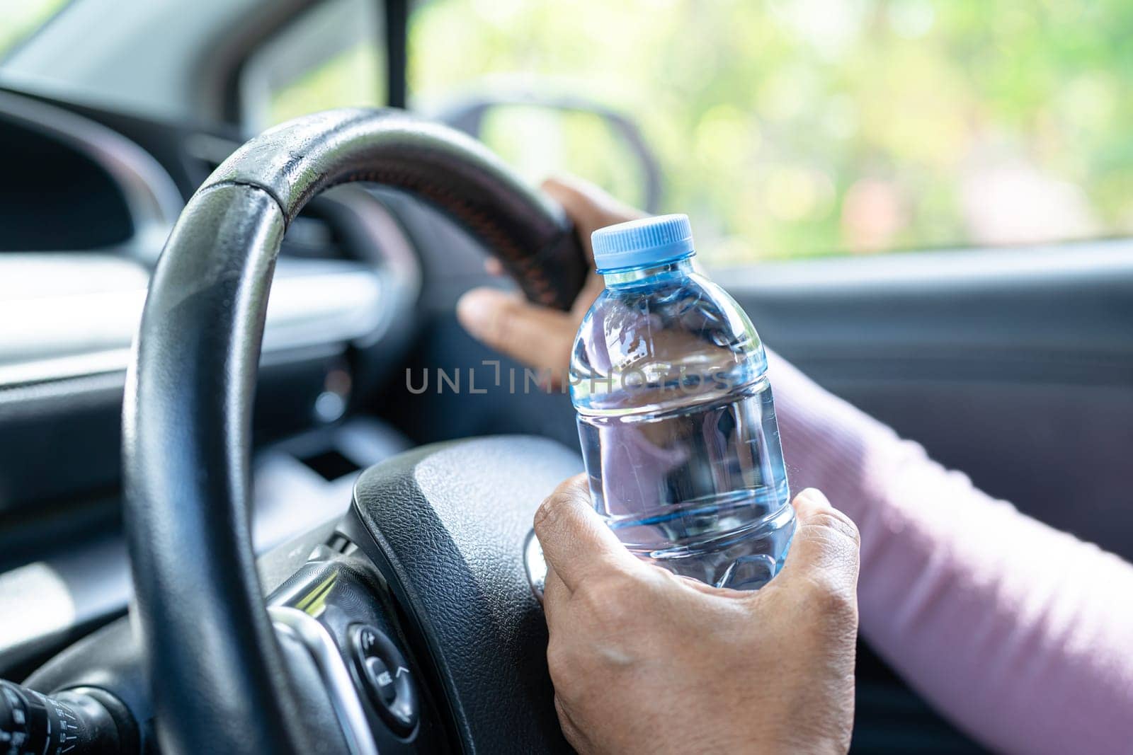 Asian woman driver holding bottle for drink water while driving a car. Plastic hot water bottle cause fire. by pamai