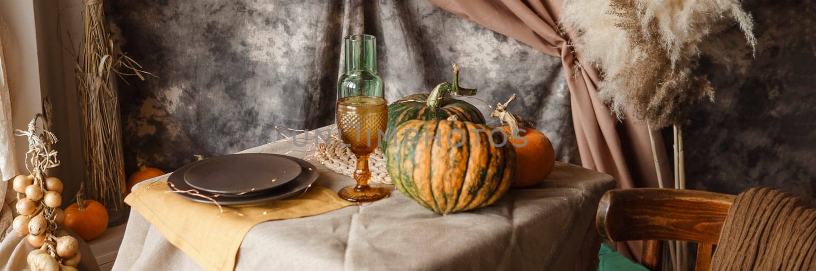 Autumn interior: a table covered with dishes, pumpkins, chair, casual arrangement of Japanese pampas grass. Interior in the photo Studio