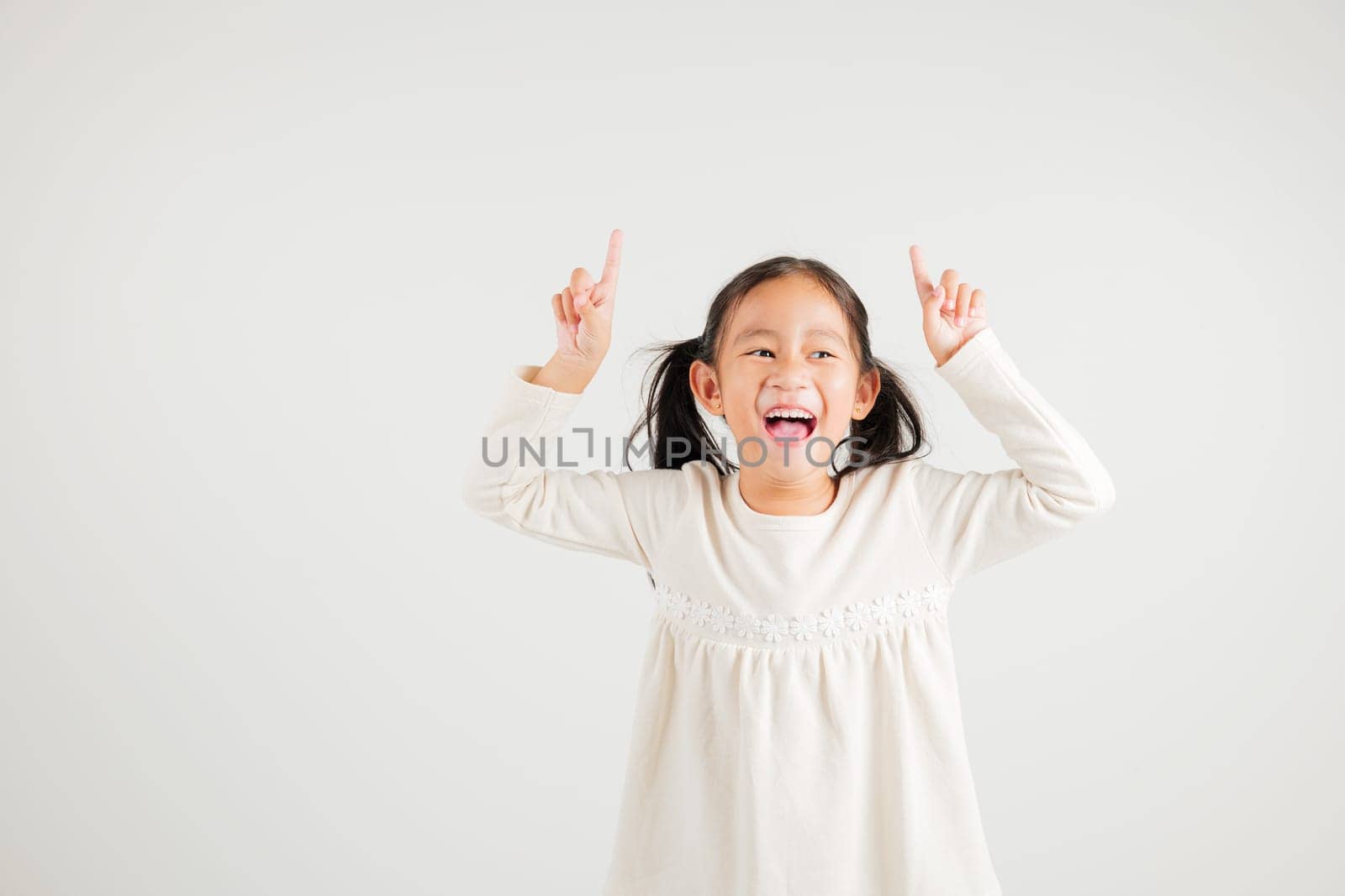 Asian happy portrait cute young kid girl makes gesture fingers point upwards above presenting product something, studio shot isolated on white background, kindergarten children woman smile