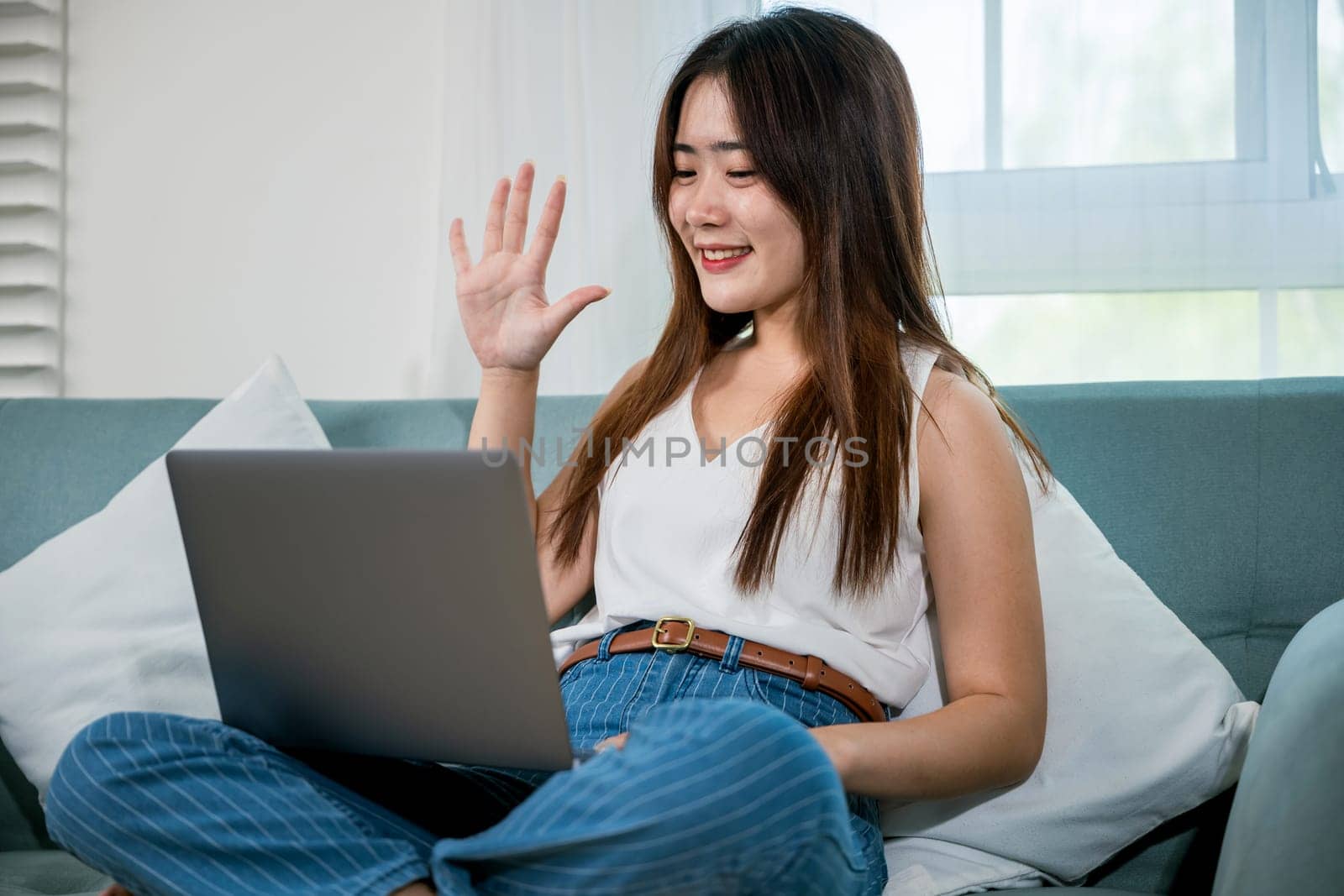 Asian young woman smiling sitting relaxing on sofa using laptop in living room at home, freelance working on computer project, Happy female typing email on notebook computer