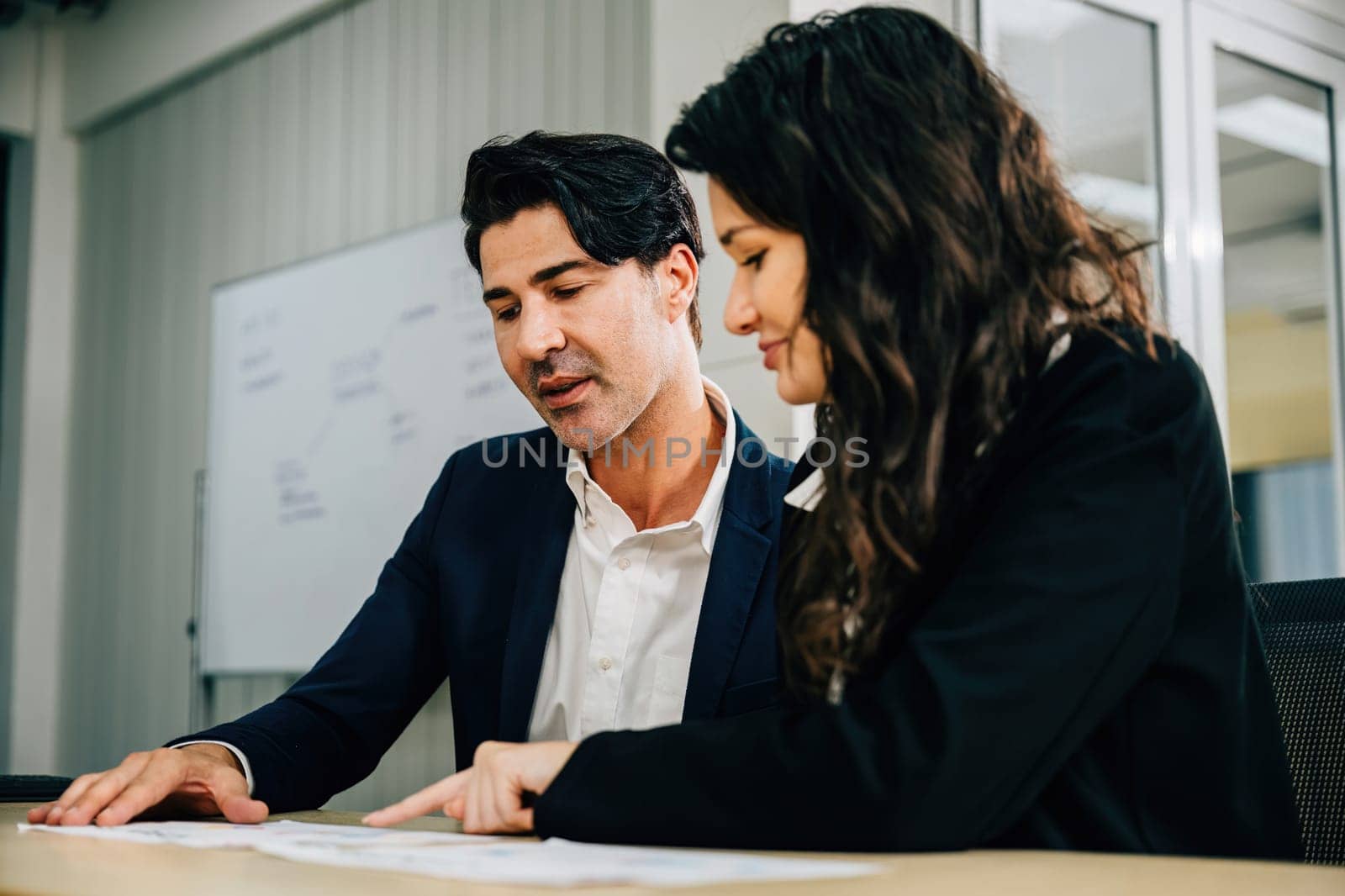 Colleagues in an office setting, working together and planning their business strategy. Teamwork is key as they discuss documents, analyze graphs, and aim for success.