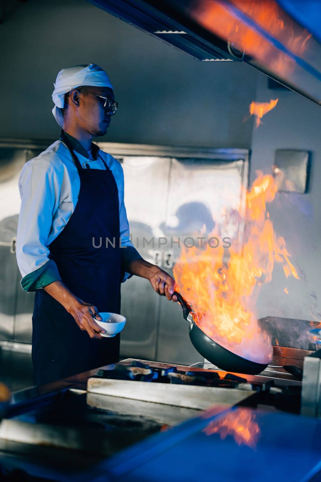 Chef hands expertly manage flaming wok in professional kitchen. Closeup of culinary skill flames cooking food. Busy chef handles flames in modern kitchen setting. cook food with fire