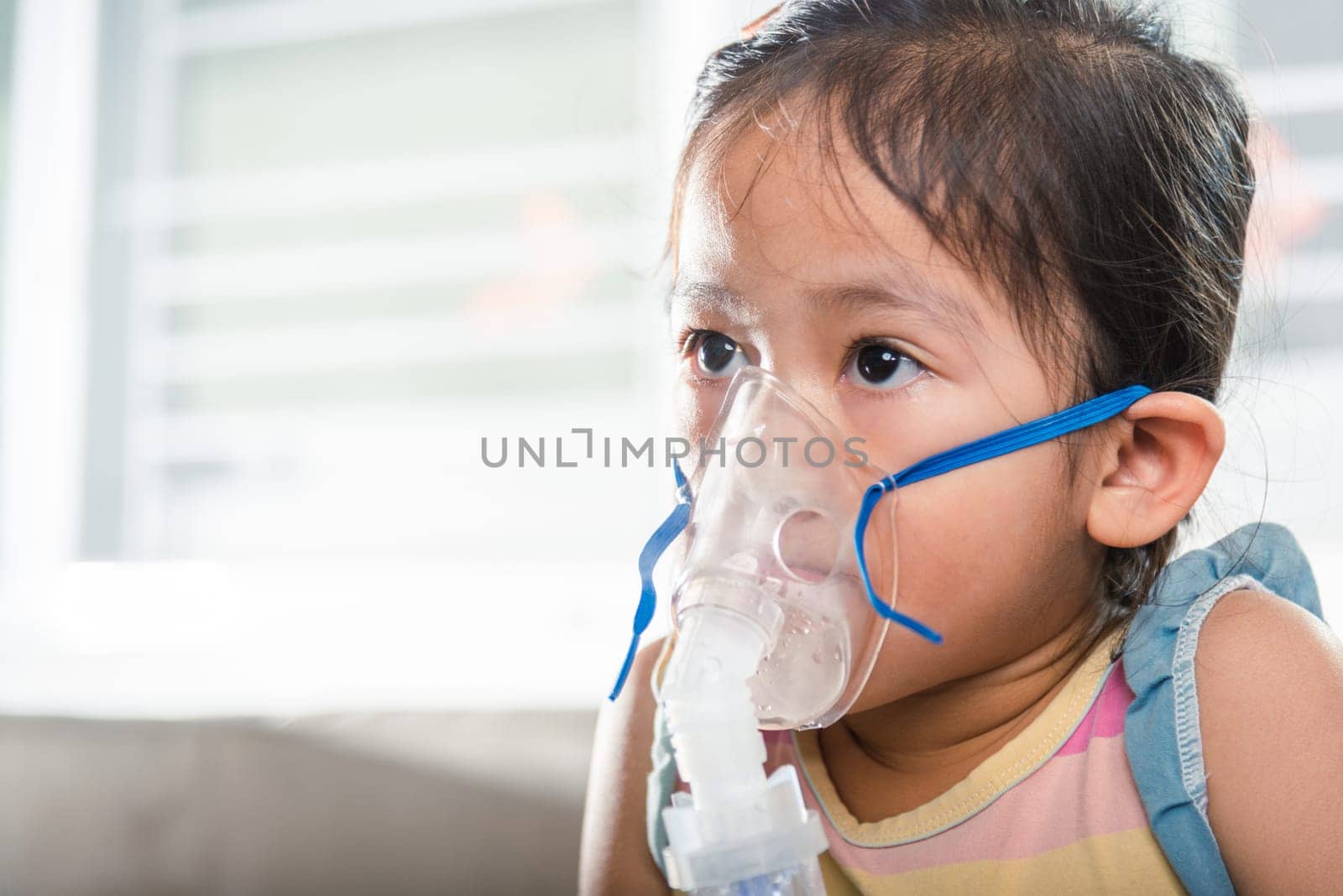 Kid girl making makes inhalation nebulizer steam sick cough at home, Asian Child using nebulizer mask equipment alone have smoke, stuffy nose and runny, oxygen spray inhaler therapy, Health medical