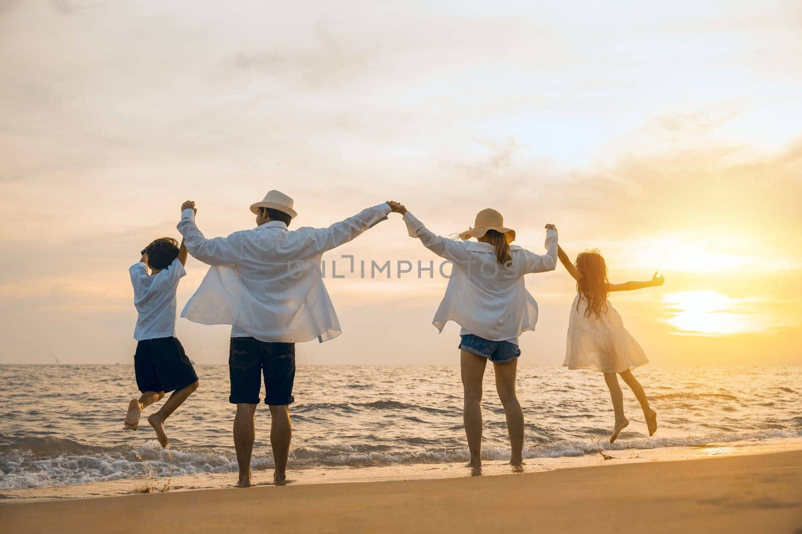 Silhouette of family holding hands live healthy lifestyle on beach, Happy Asian family have fun jumping together on beach in holiday sunset time, Back people enjoying travel trip and summer vacations