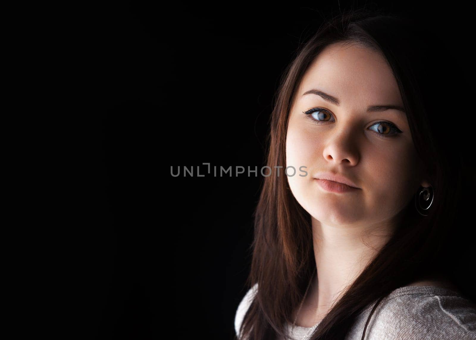A young woman with long brown hair displays a calm and thoughtful expression. She is positioned in front of a dark background, accentuating her features and soft expression.