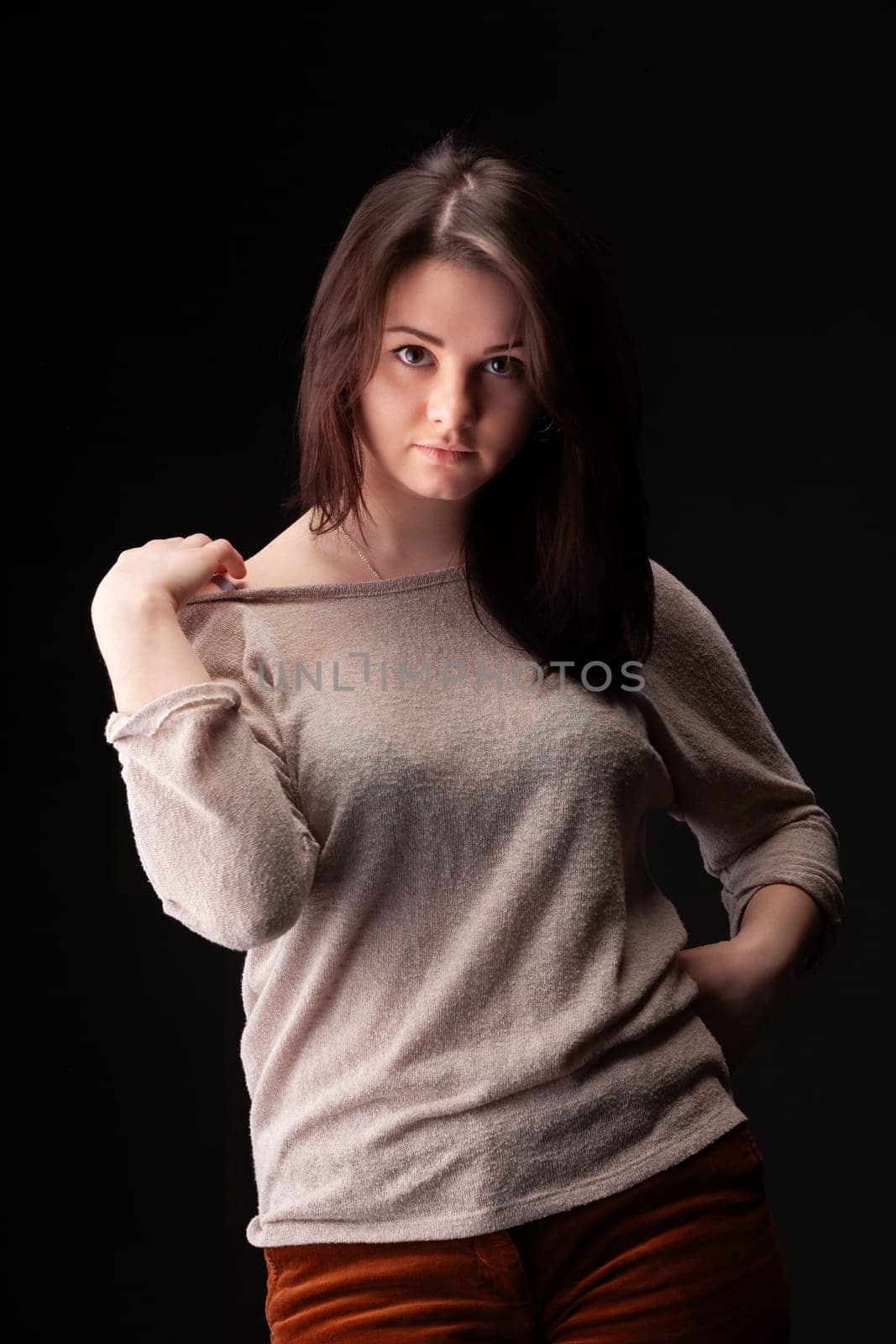 A female model stands poised in a studio, showcasing confidence and elegance. She wears a light sweater and interacts playfully with her clothing, creating a striking visual effect.