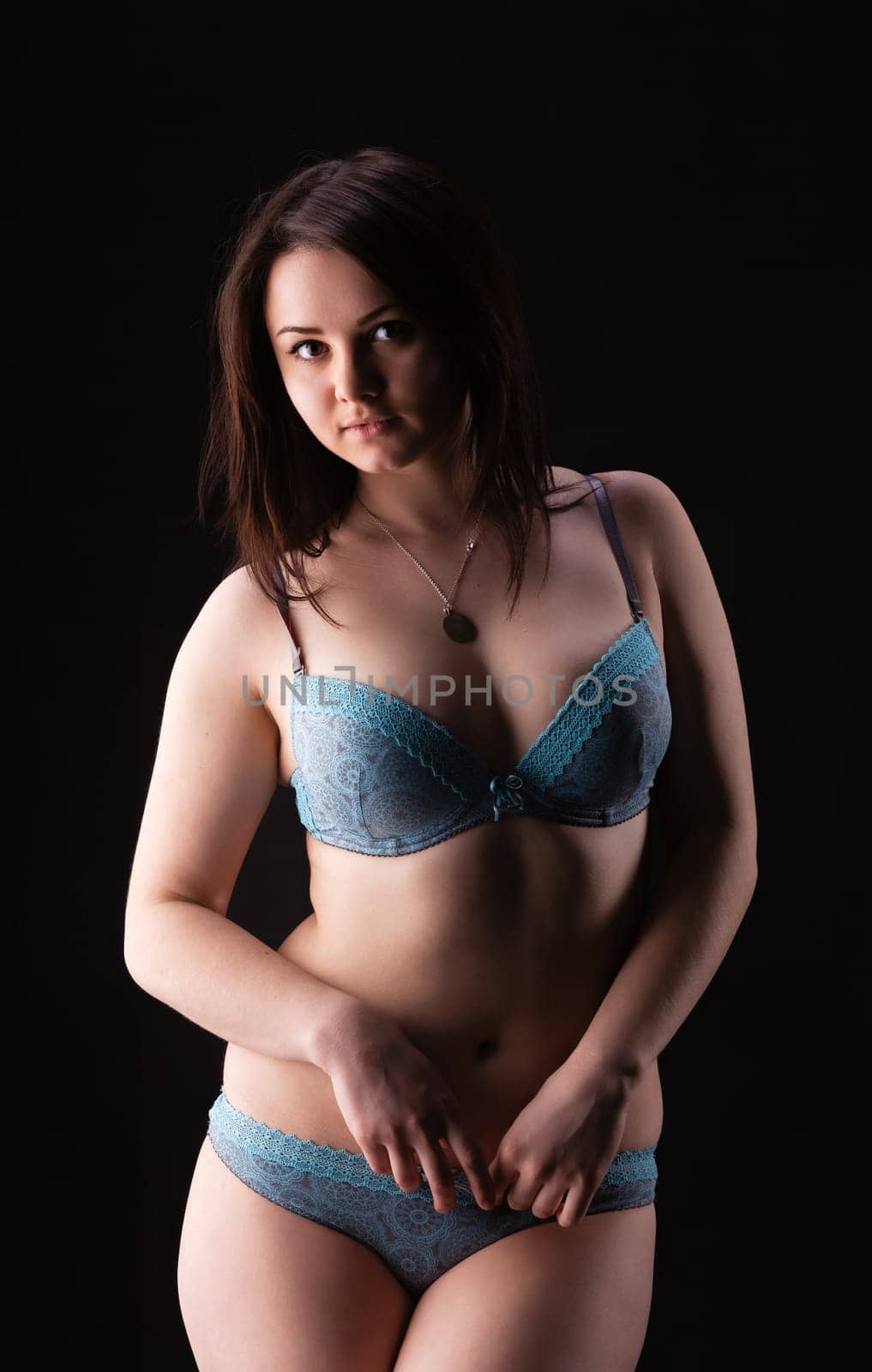 A model is showcasing intimate apparel, featuring a delicate blue design, in a studio with a dark backdrop. The soft lighting highlights the models features and pose.