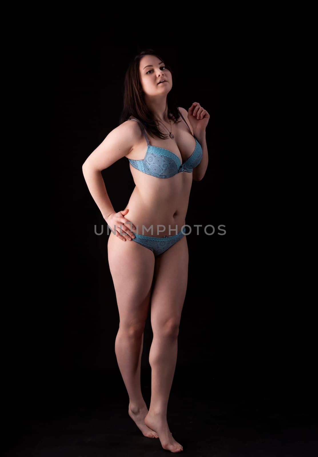 A model showcases blue lingerie while striking a confident pose in a studio with a dark background. The focus is on body positivity and self-expression through fashion.