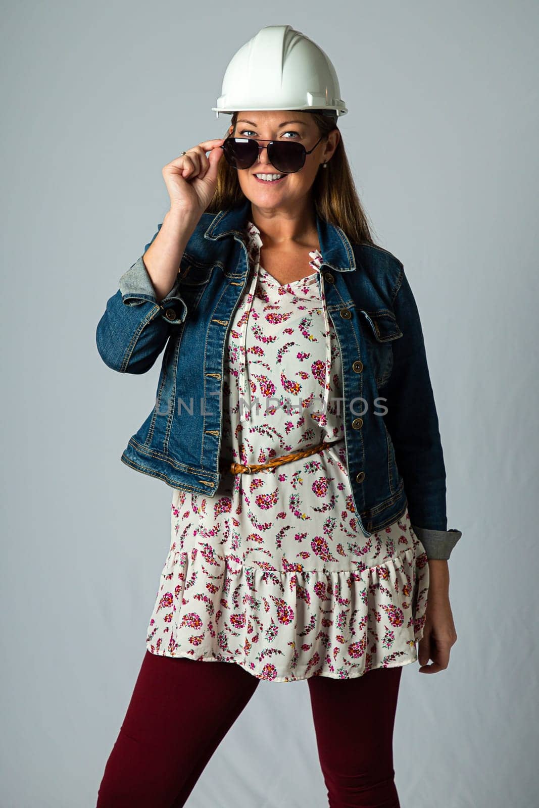Forty something woman, wearing casual clothes, hard hat and sunglasses, holding her demin jacket
