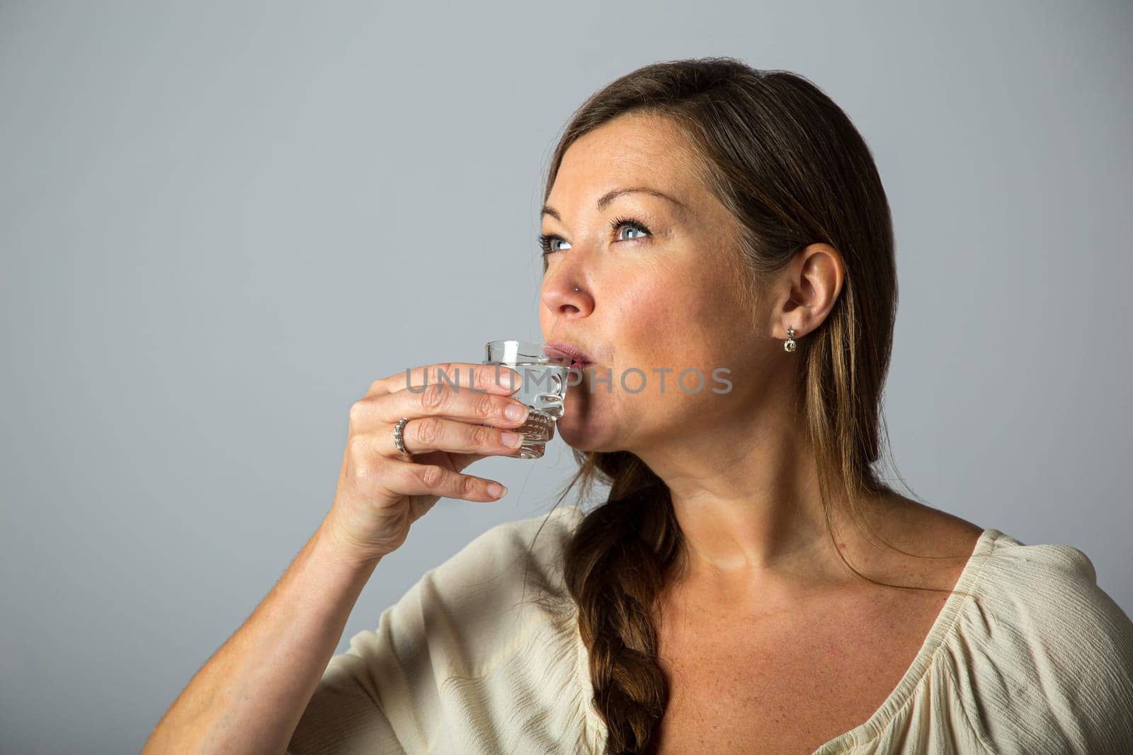 Forty something woman, wearing casual clothes, drinking alchool from a shooter glass
