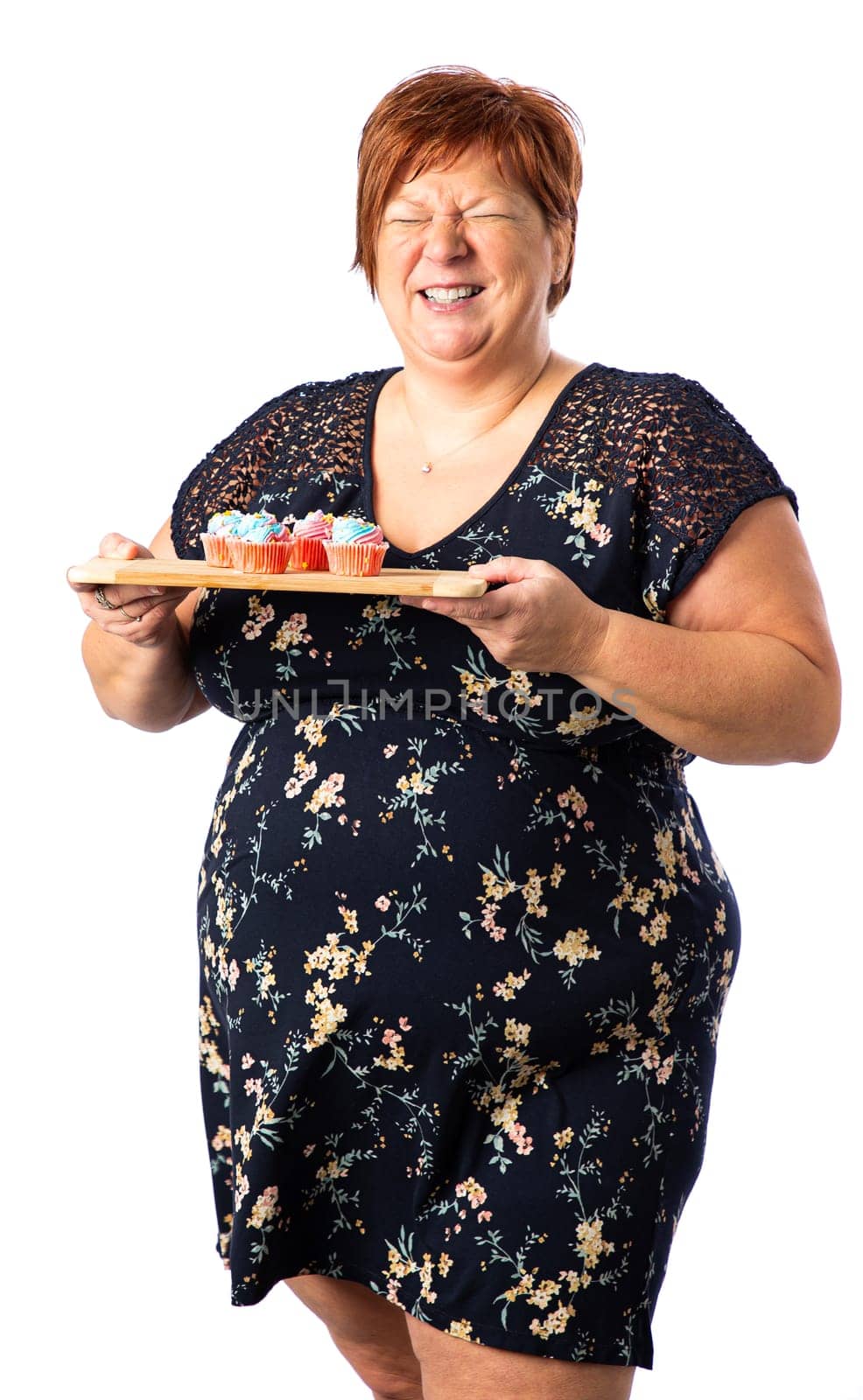 Fifty something woman laughing while holding a plate of small colorful cupcake