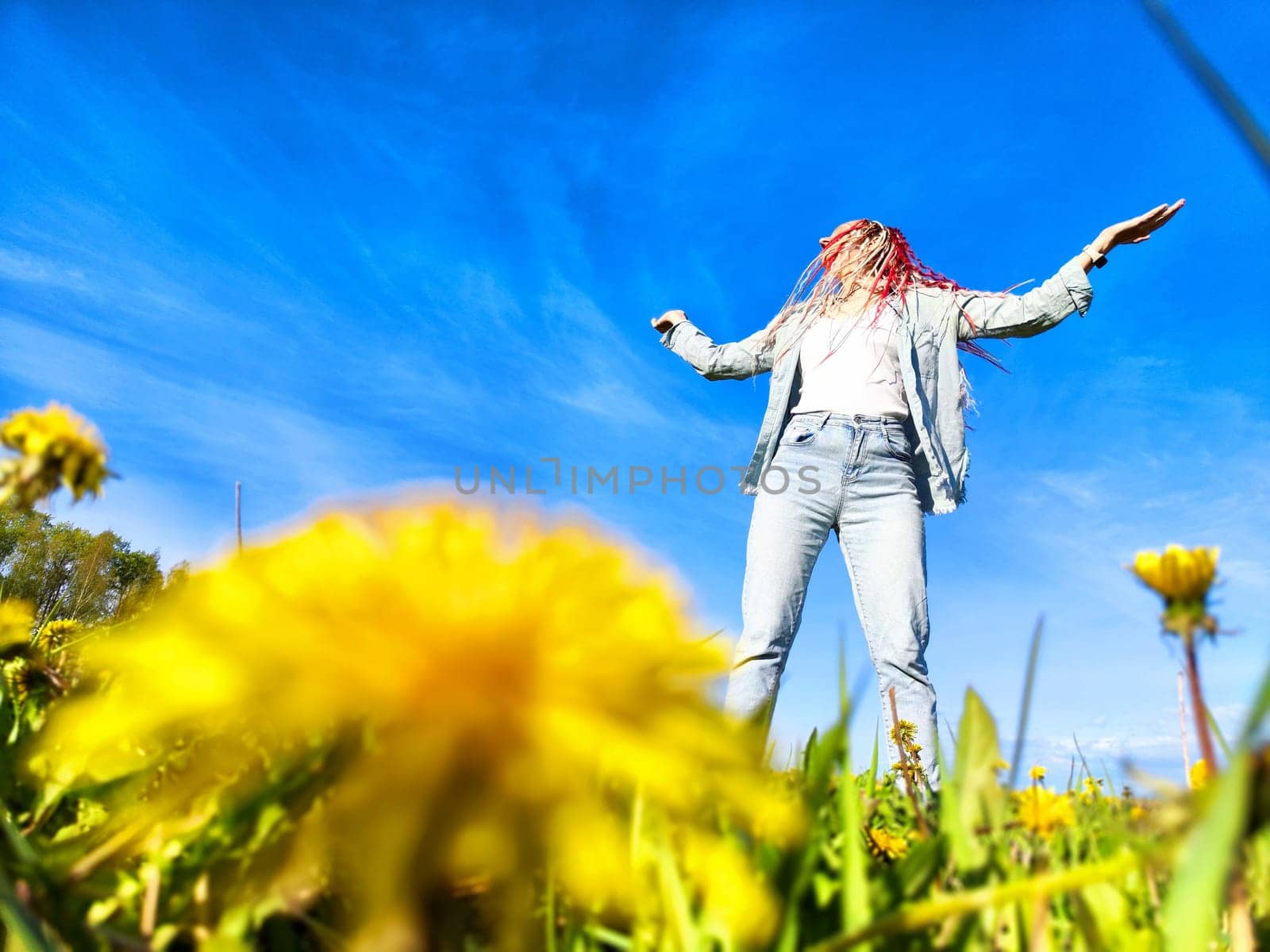 In a sunny field filled with dandelions, an individual joyfully dances, embracing the beauty of nature and the bright blue sky.