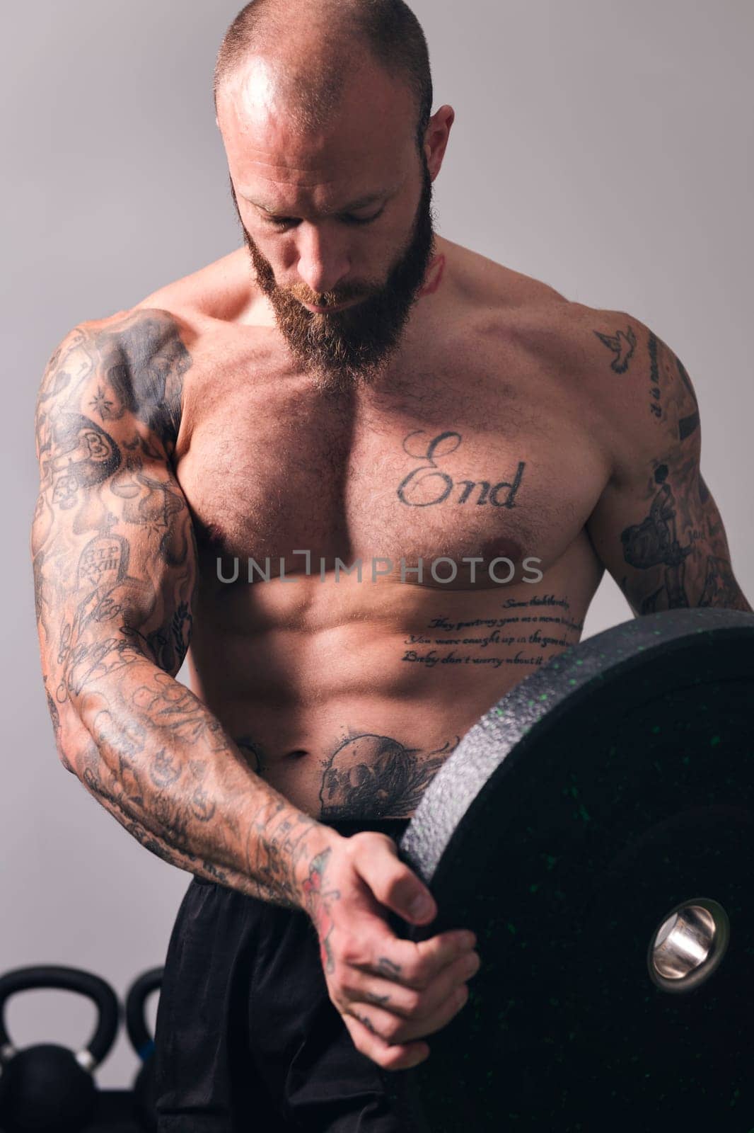 sportsman with muscular body and naked torso standing with heavy weight plate during workout in gym, concept of fitness and active lifestyle