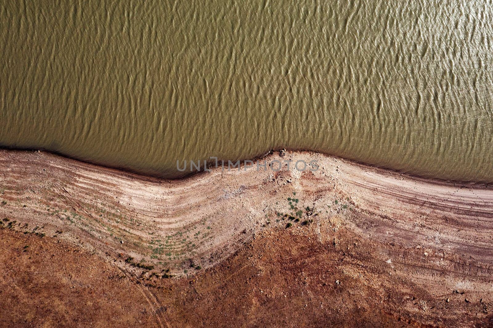 drone view of river with rippled water surface flowing near stony shore with dried surface in nature, concept of environment and ecology