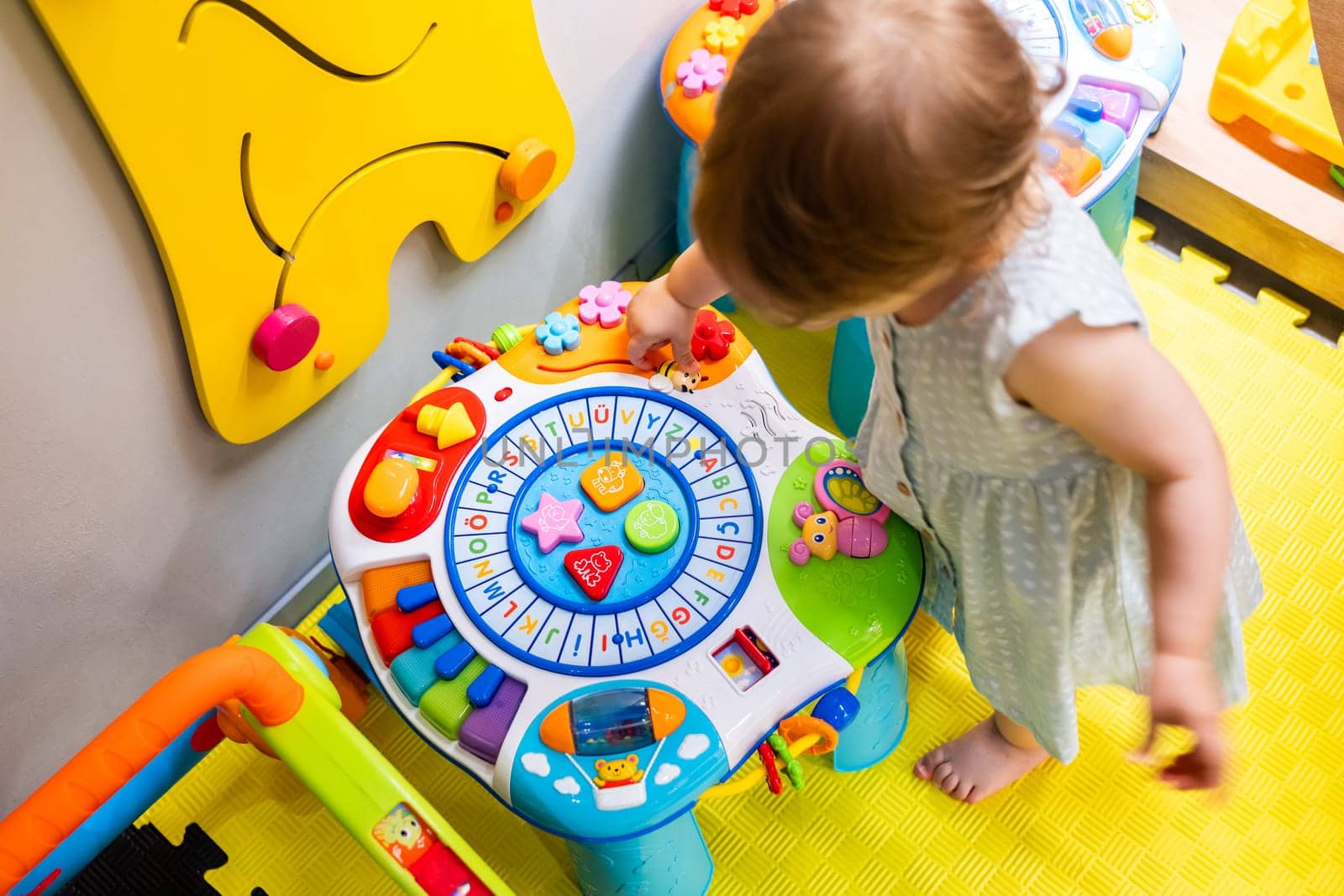 Child engaging with an educational toy table in a vibrant playroom, exploring shapes and colors. Concept of joyful learning and encouraging creativity in early childhood