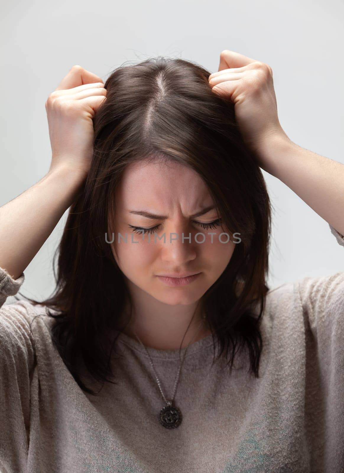 A young woman with brown hair holds her head in her hands, looking stressed and distressed.