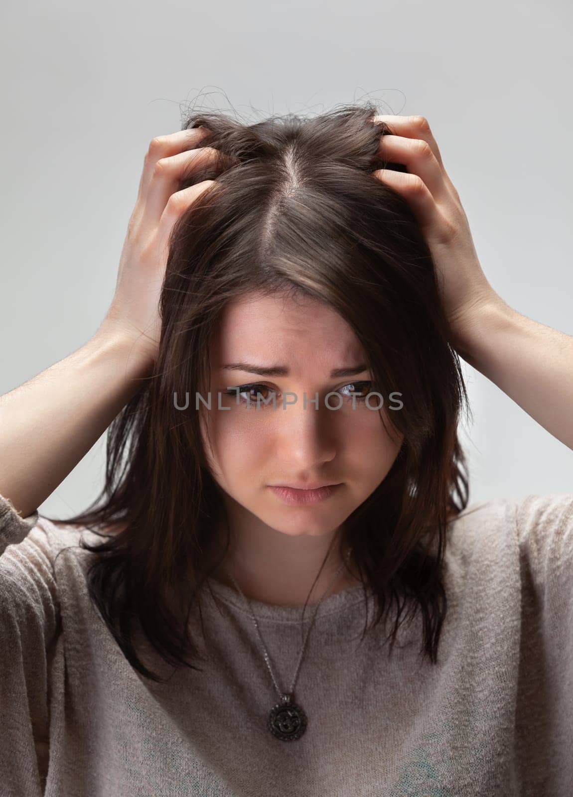 A young woman with brown hair holds her head in her hands, looking down with a troubled expression.