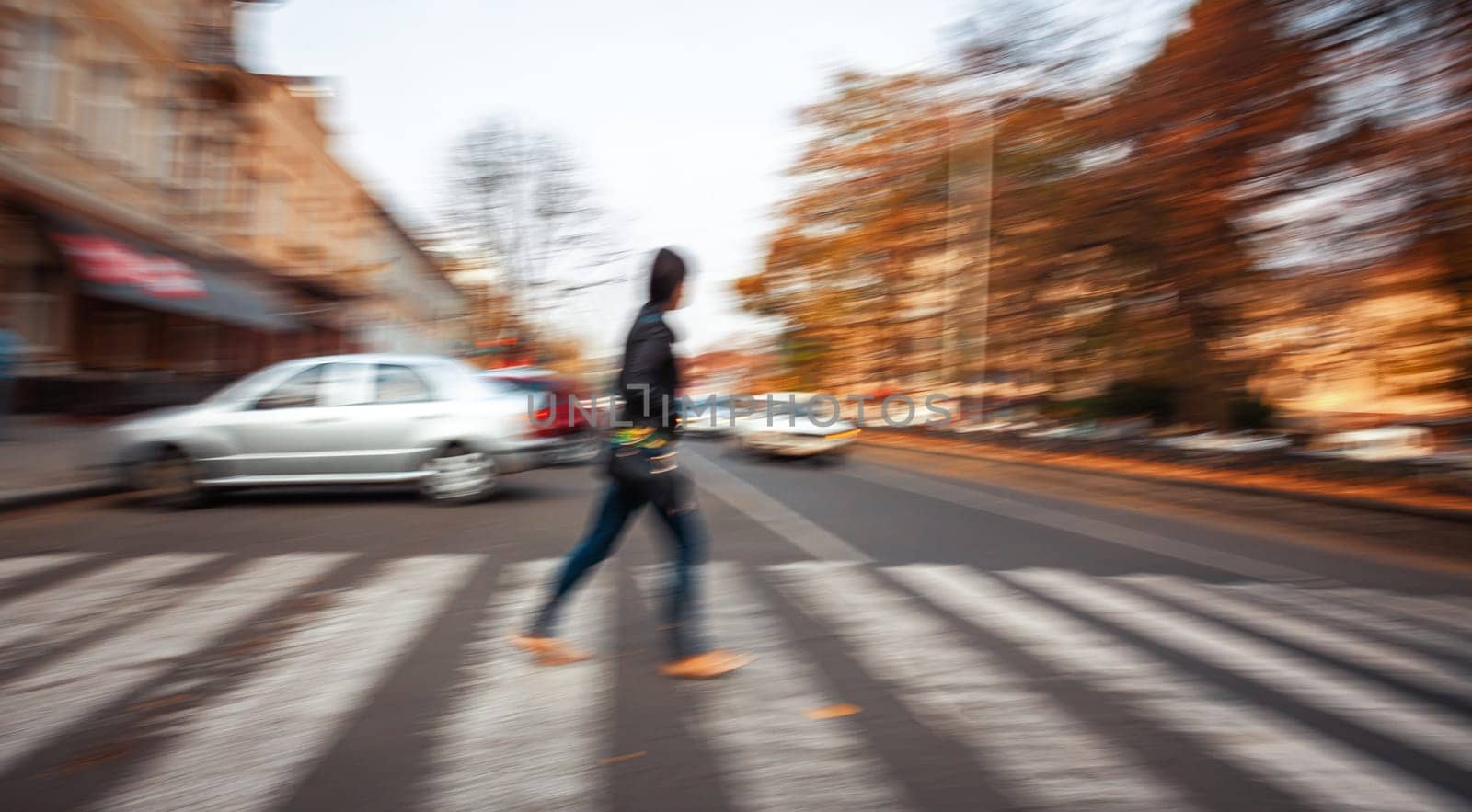 A person walks across a city crosswalk as cars speed by in a motion blur.