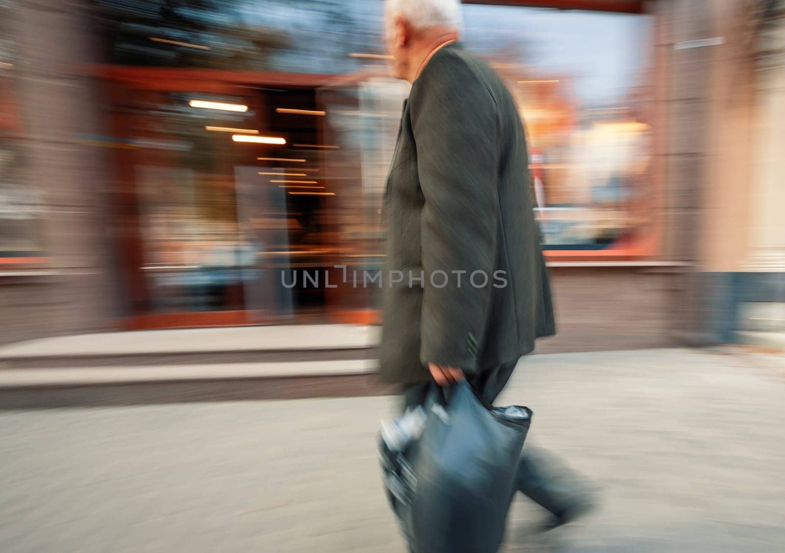 A man in a suit walks briskly down a city street, past a blurred storefront.