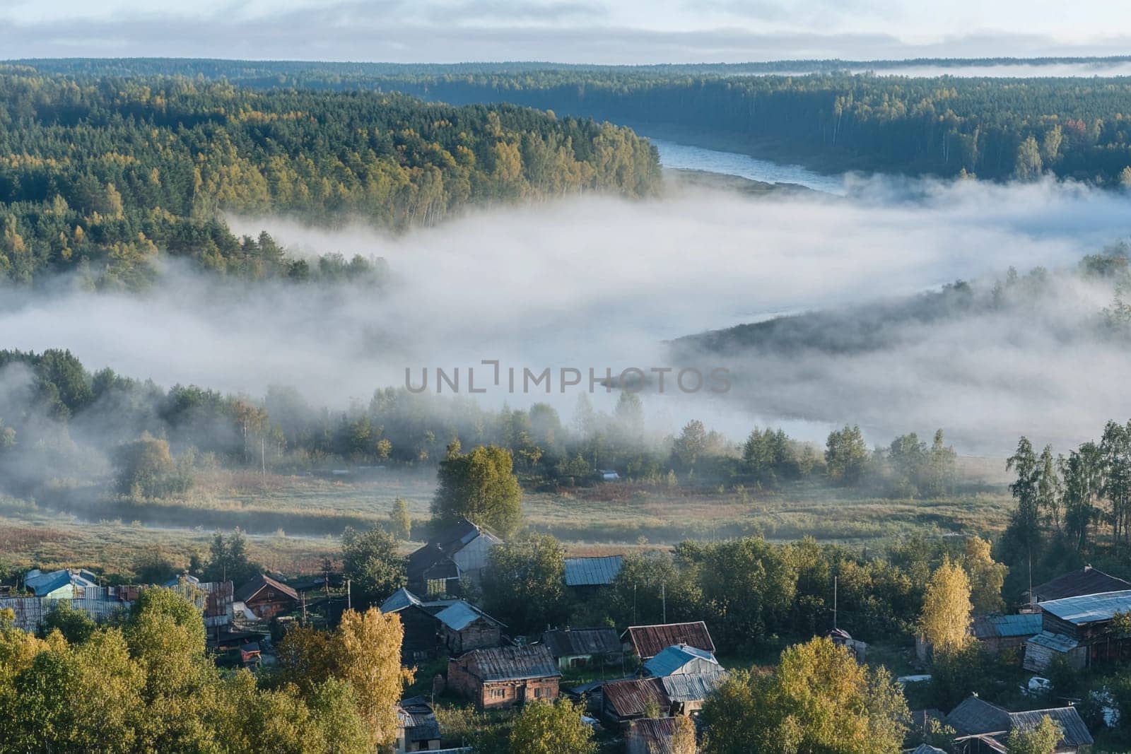 Early morning fog envelops a quiet village along the river, creating a serene atmosphere in the surrounding forested landscape.