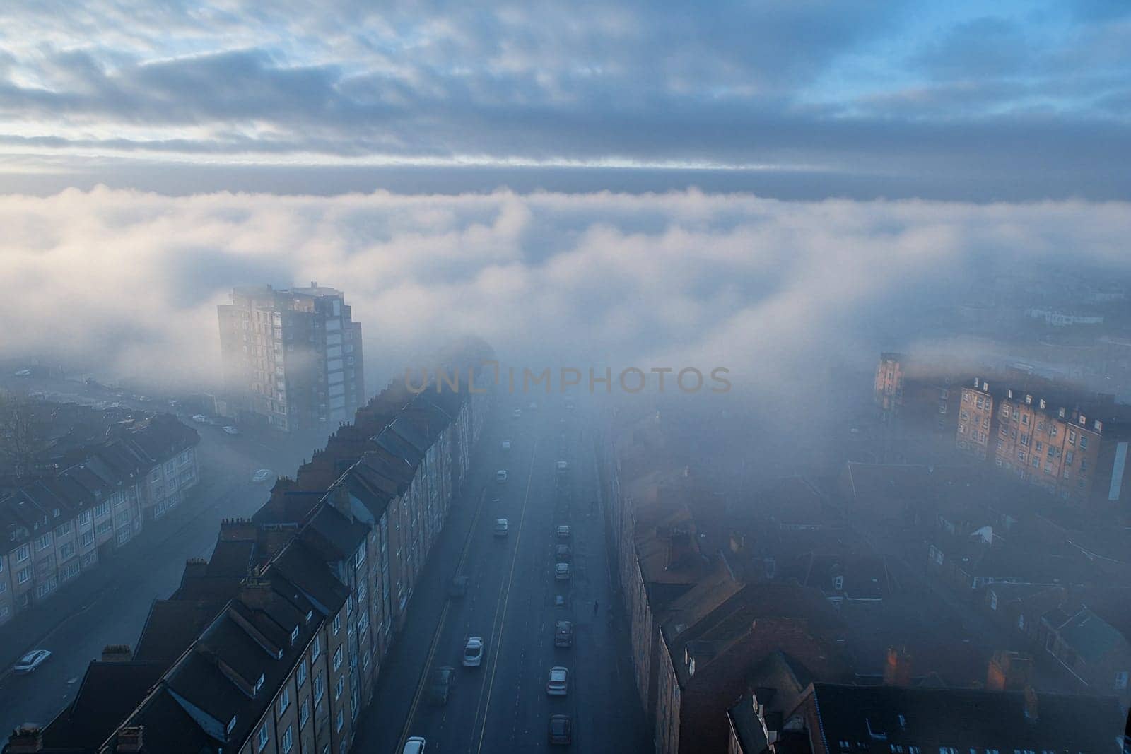 Thick fog envelops the city skyline, shrouding buildings and streets while creating a tranquil and mysterious early morning landscape.