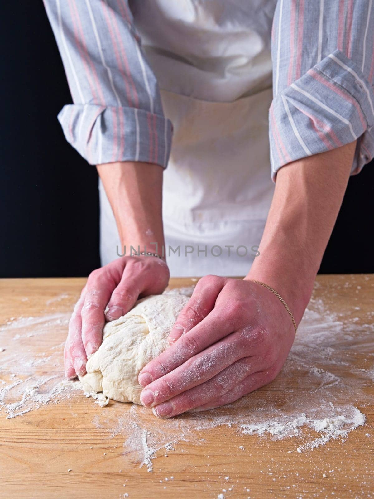 A close up photo of the hands of a man forming dough into a ball on a wooden table.