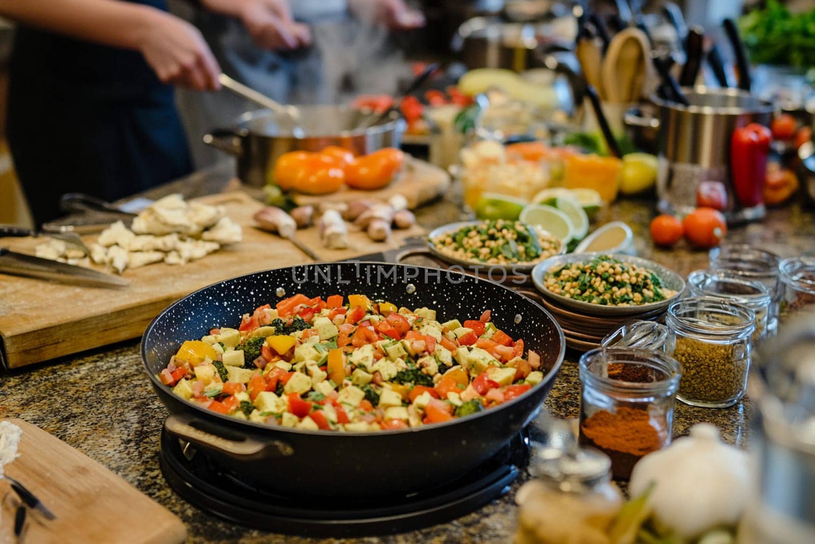 Fresh vegetables sizzle in a pan while various ingredients fill a busy kitchen counter, creating an atmosphere of culinary creativity.